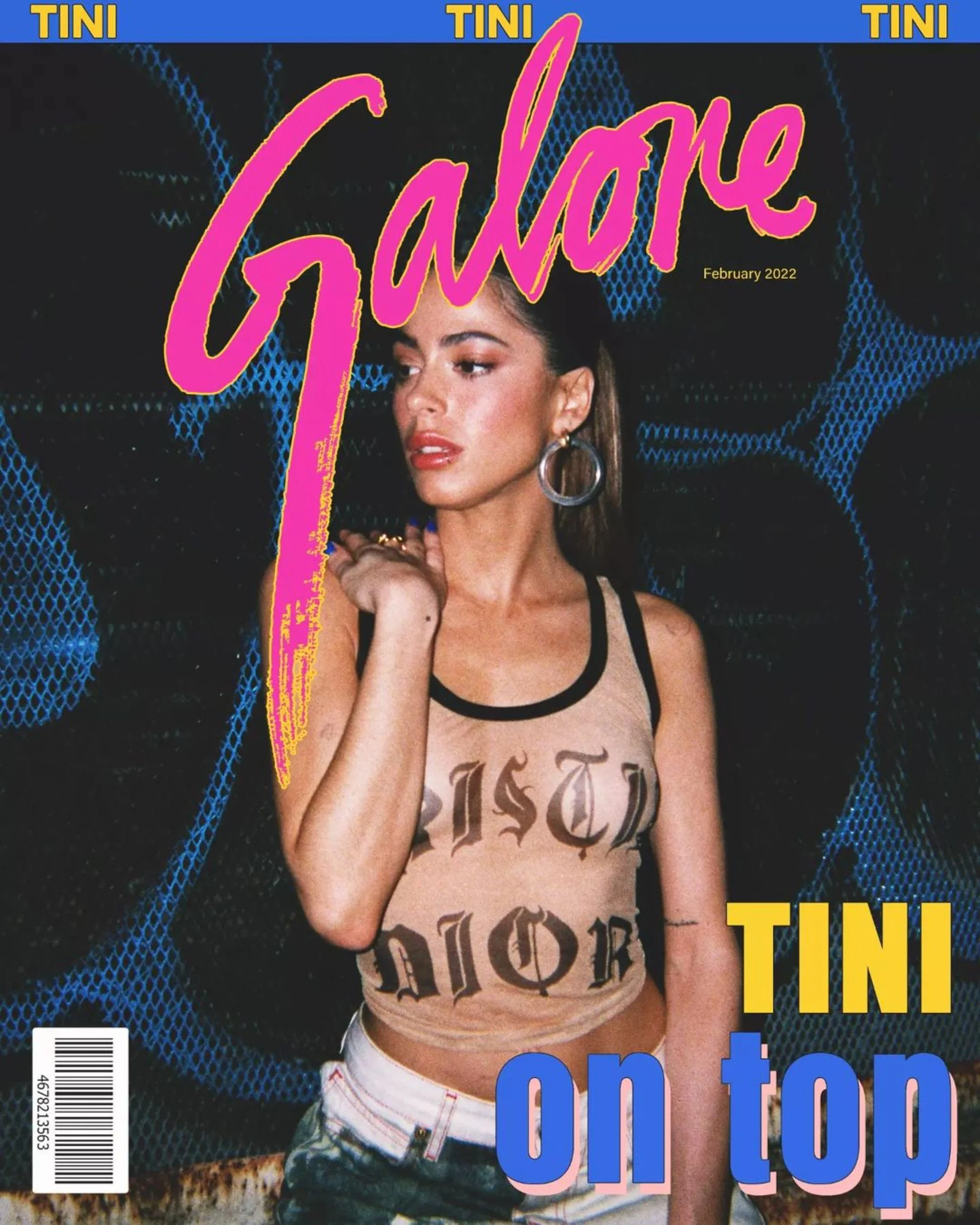 Magazine cover featuring Tini, a young woman with brown hair, wearing a see-through tank top with 'written on it, and light-colored jeans. She is posing against a dark, textured background with blue highlights, wearing large hoop earrings and makeup.
