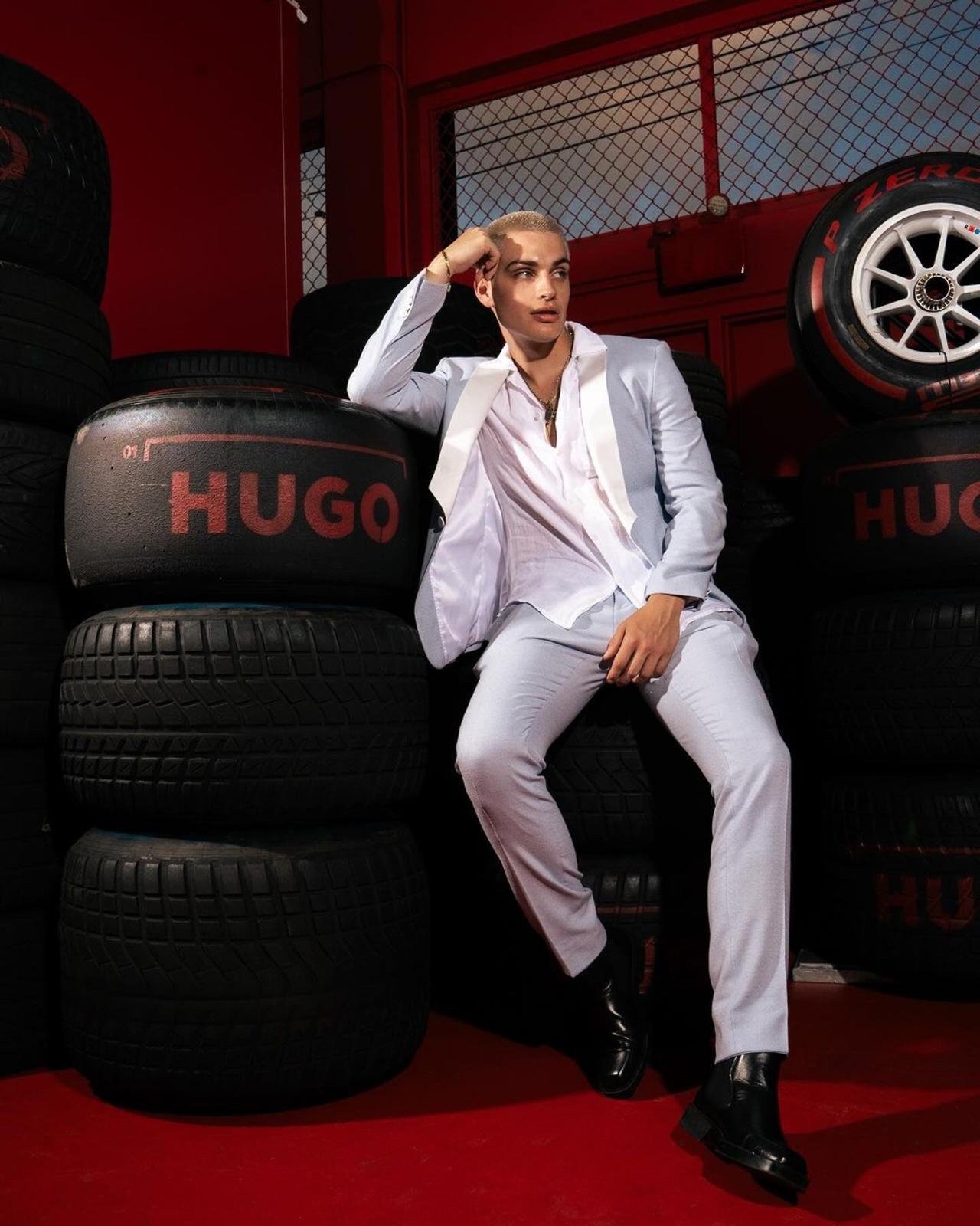 Person dressed in white clothing sitting on black tires with red and black background, with the word 'HUGO' printed on the tires.