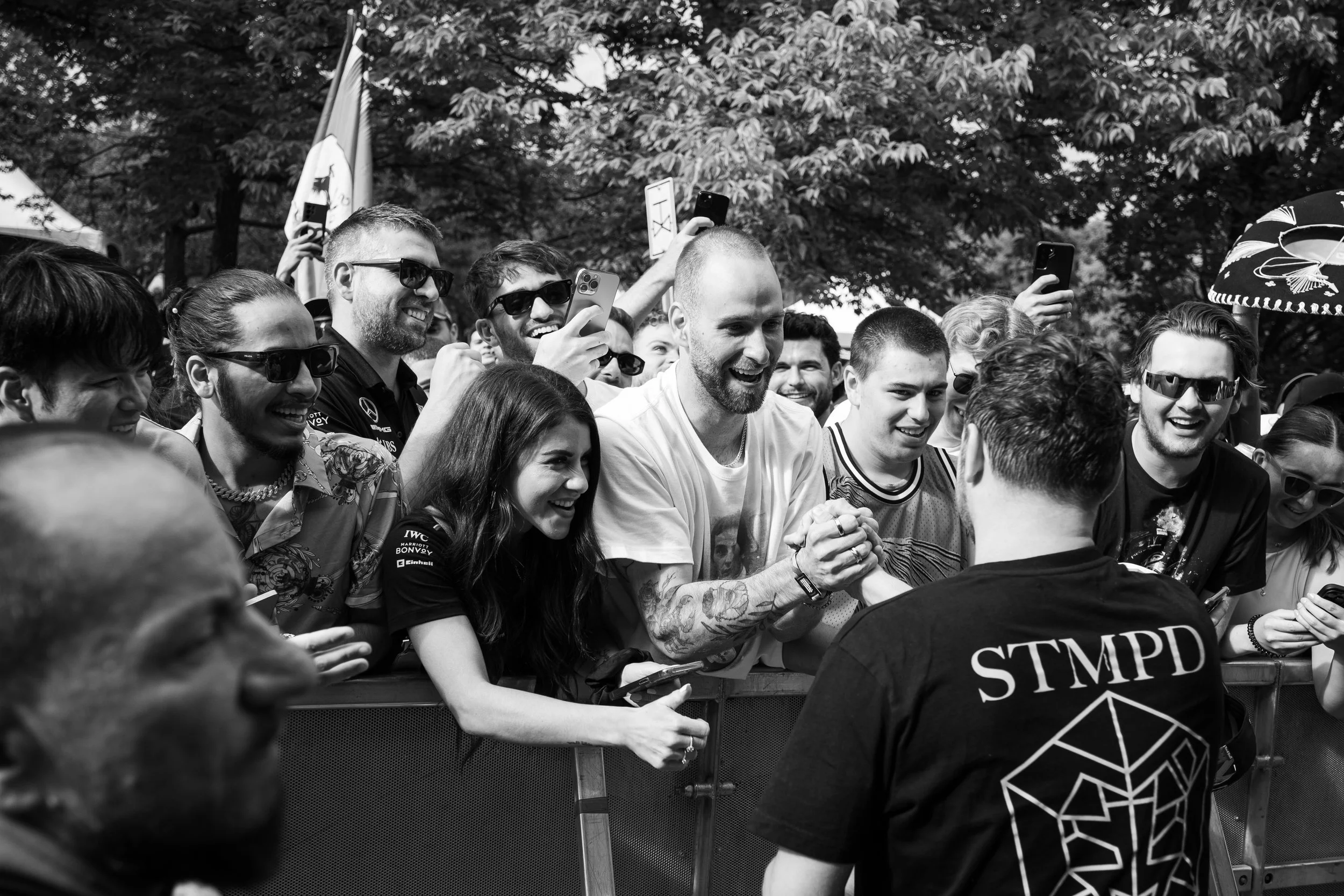 A crowd of people at an outdoor event, with many smiling and taking photos. A man with a beard and tattoos is shaking hands with a person wearing a shirt with 'STMPD' on the back.