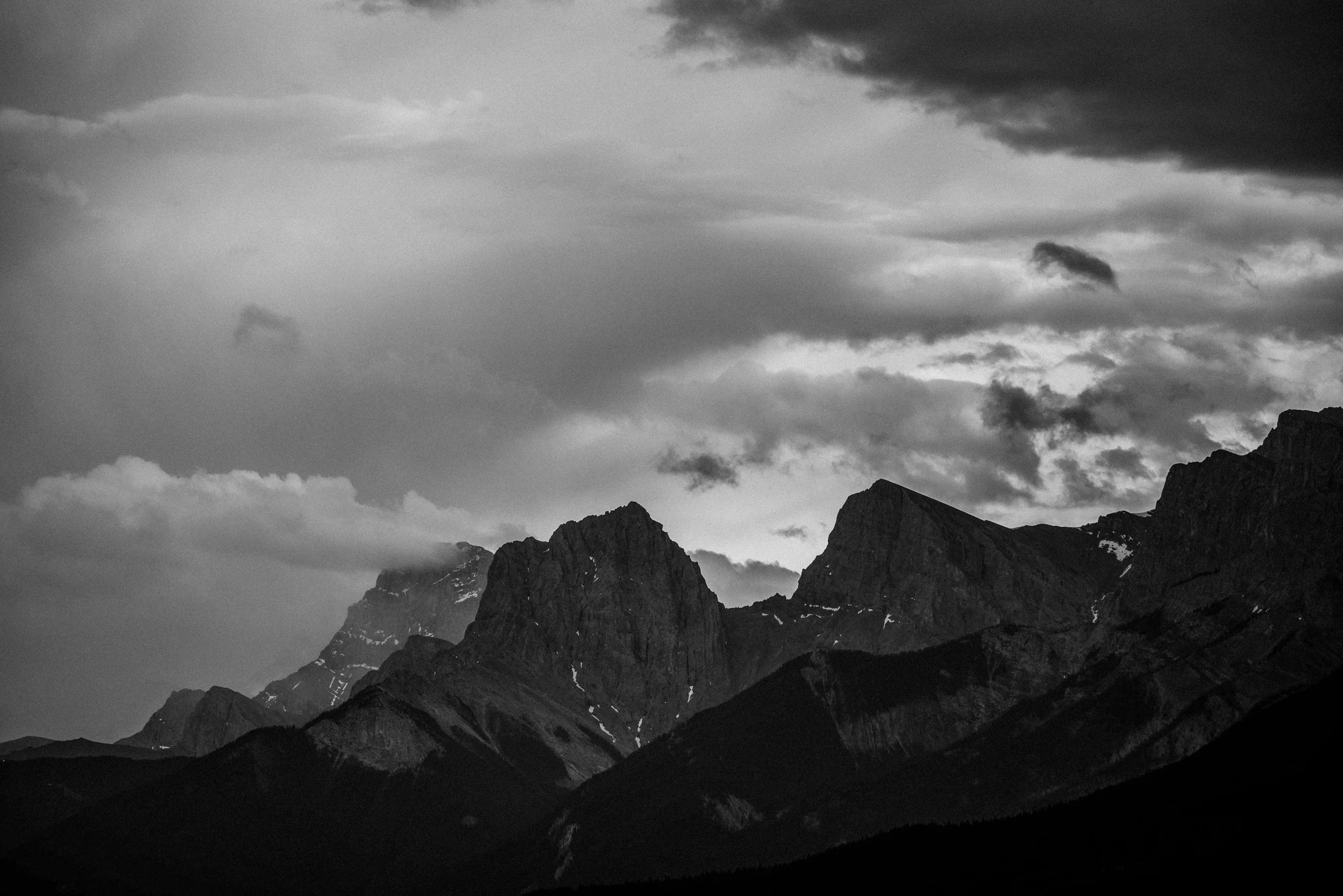 Black and white photograph of mountain range with dramatic clouds overhead.