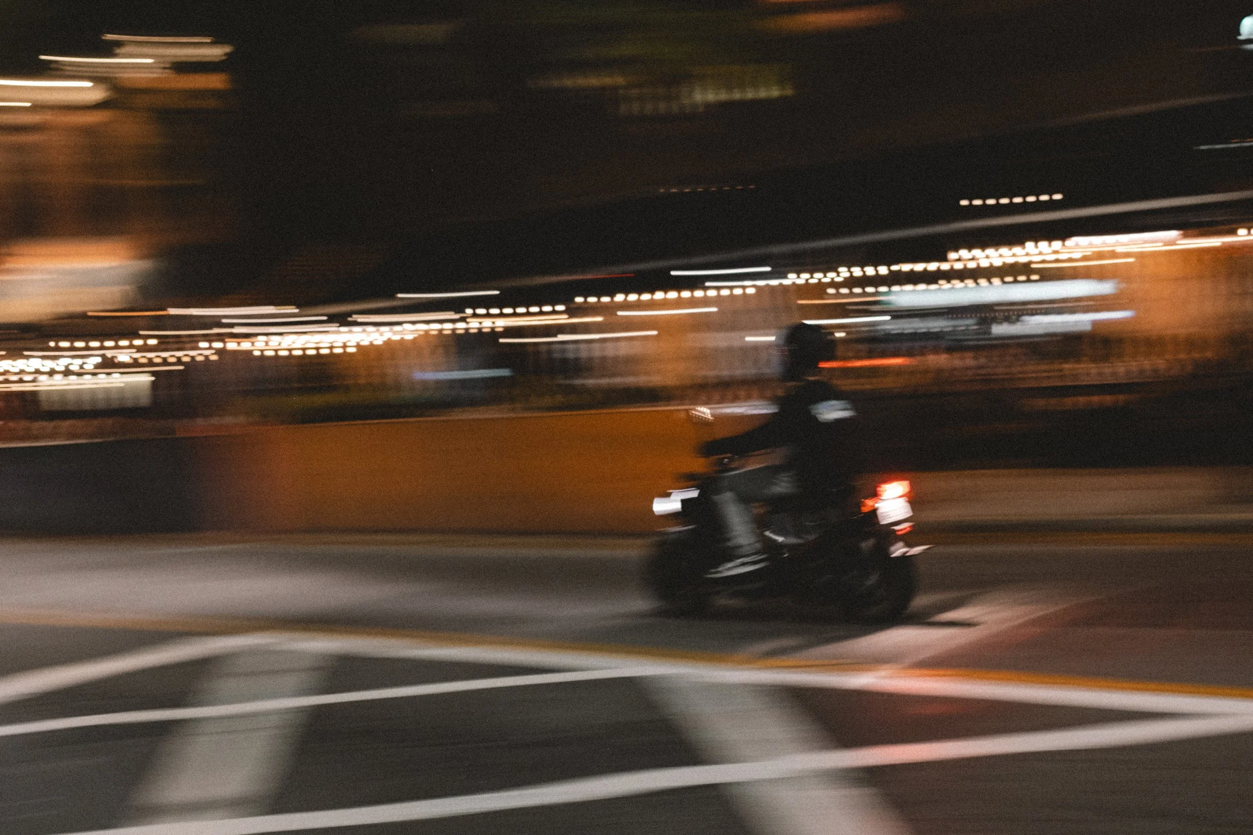 A person riding a motorcycle at night on a city street, motion blurred with city lights in the background.