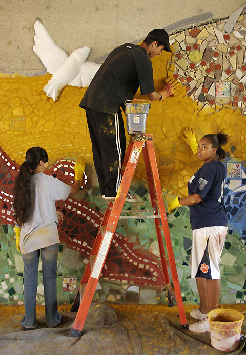 Youths complete the bricolage mosaic by grouting it.