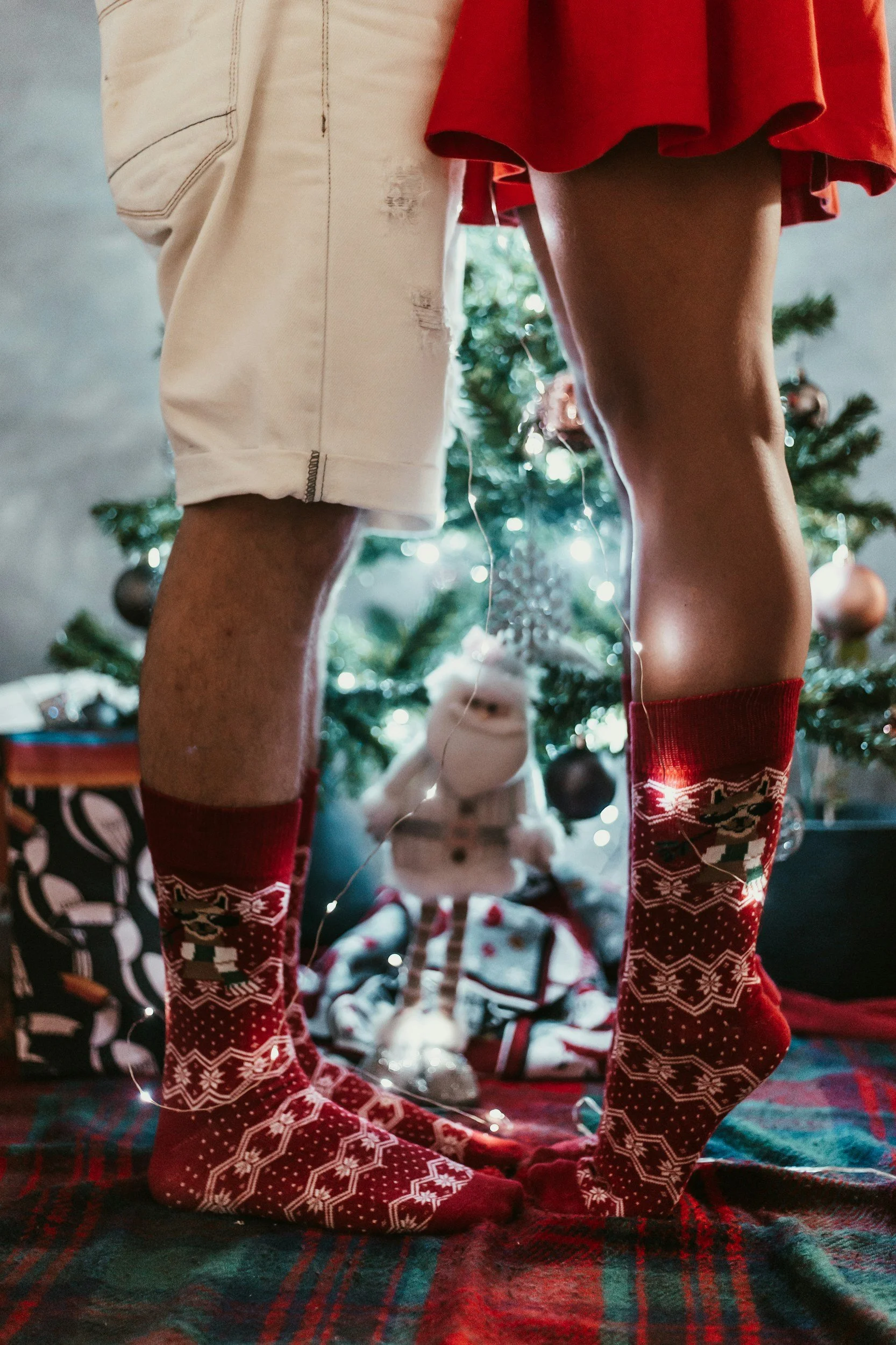 Couple wearing festive Christmas socks standing together by a decorated Christmas tree