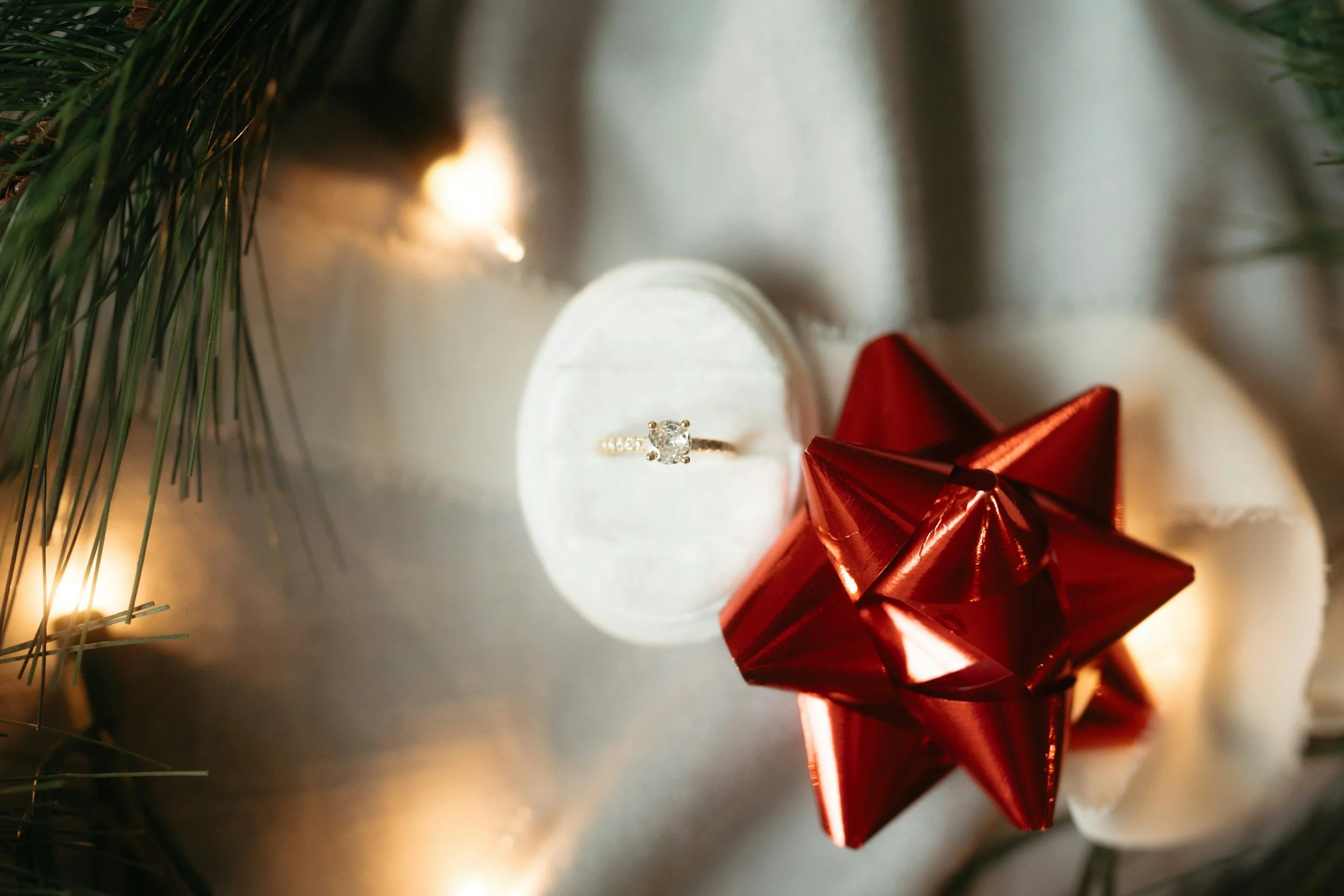 Engagement ring displayed with a red Christmas bow and festive lights, perfect for a holiday proposal