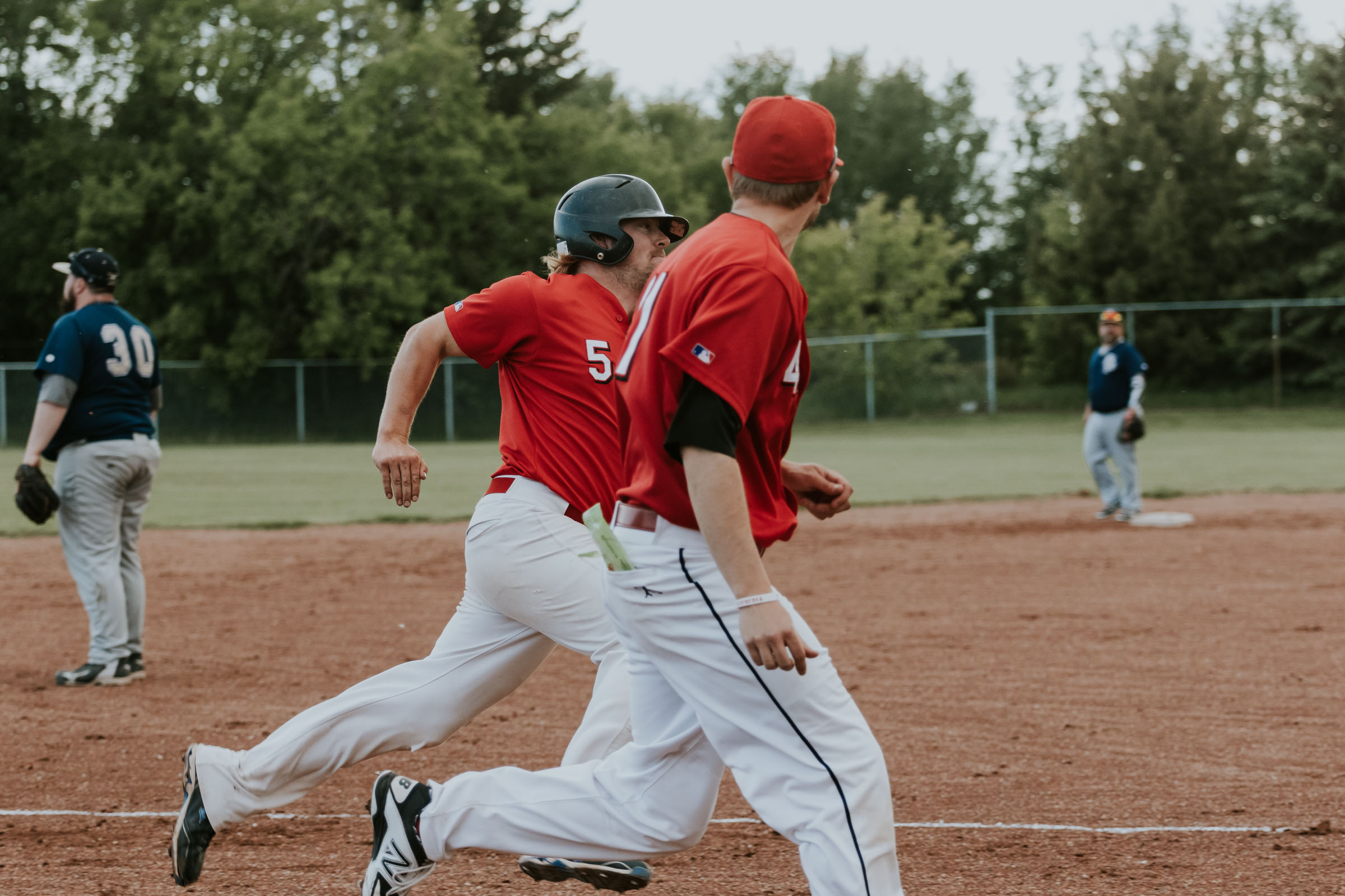 There is nothing like support from a teammate. In this case Camrose Axemen outfielder Blair Mulder (5) gets encouragement all the way down the third base line from reliever and third base coach Kyle Muzechka | June 1 at Archie Jenkins Field, Bon Accord