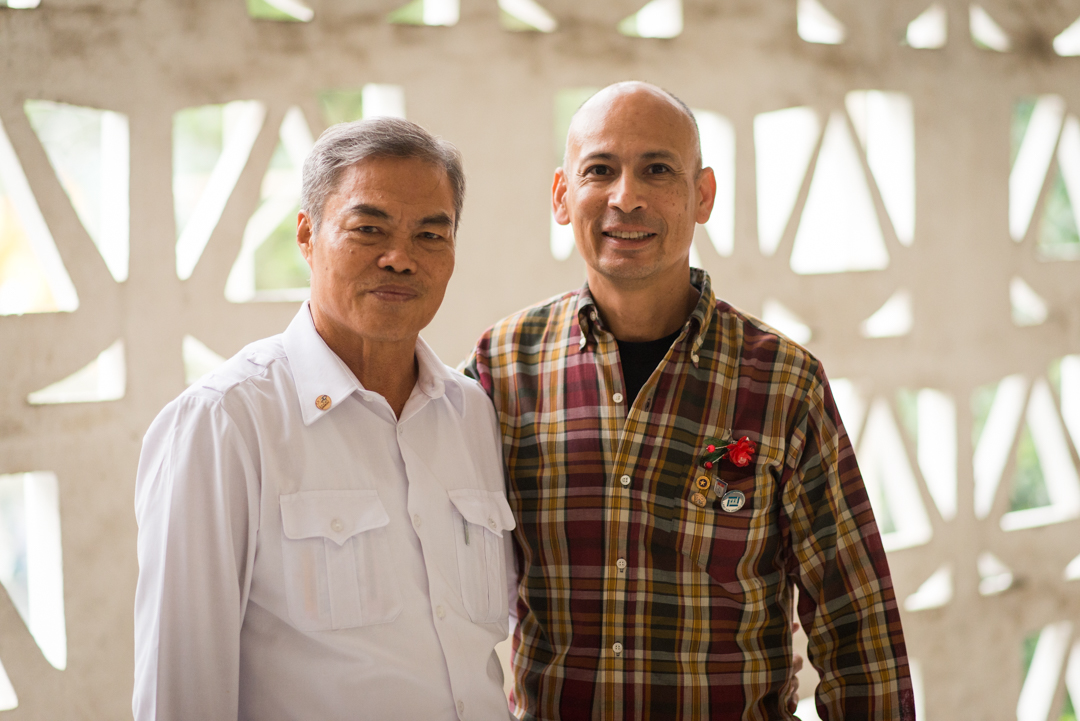 Mr. Xiem with Ron Reyes after the meeting. Mr. Xiem wears the 2 Sides Project lapel pin, as does Ron Reyes, along with his Gold Star pin. Ron also wears a red flower pin. It was made by victims of Agent Orange. Mr Xiem gave each of us a flower pin. Photo courtesy Istrico Productions.