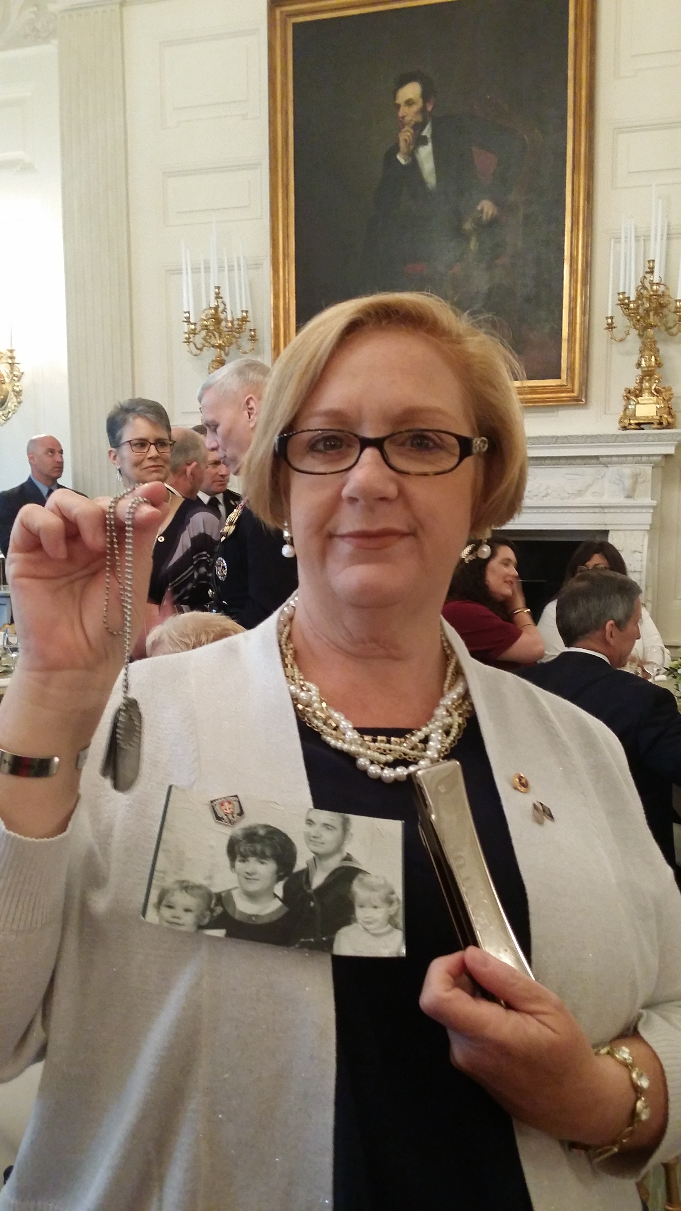 Susan in the Lincoln Room of The White House, where breakfast was held. Her father's harmonica, which was returned from Vietnam, is in her left hand. The dog tags she holds in her right hand, a gift from Jeanette Chervony, bear the names of the fathers of the first six who went on the 2 Sides Project trip to Vietnam. Photo courtesy Susan Mitchell-Mattera.