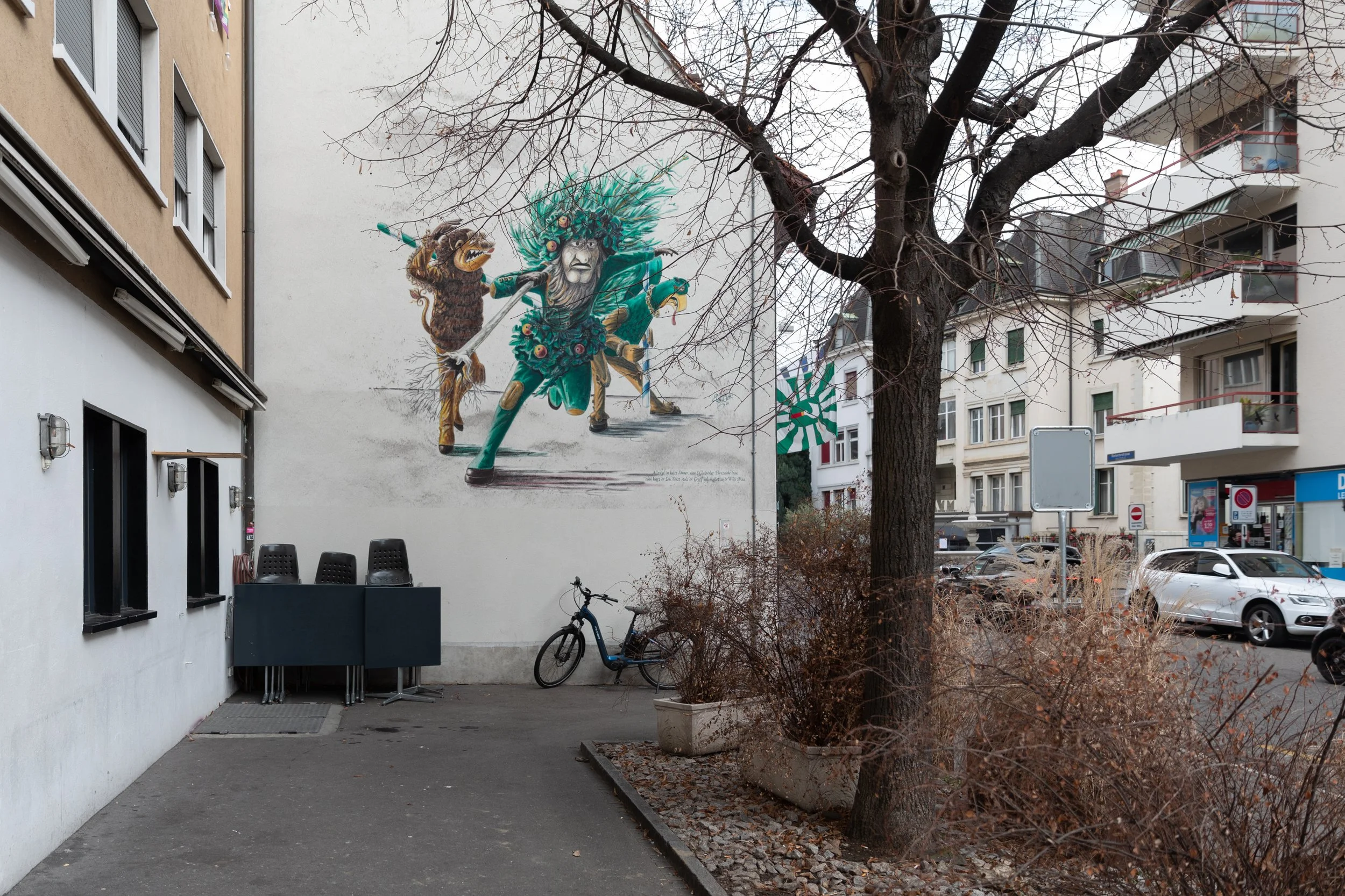 Wandgemälde eines mystischen Kriegers in grüner Kleidung mit einer Tierbegleiterin, an einer weißen Gebäudemauer in einem urbanen Gebiet.