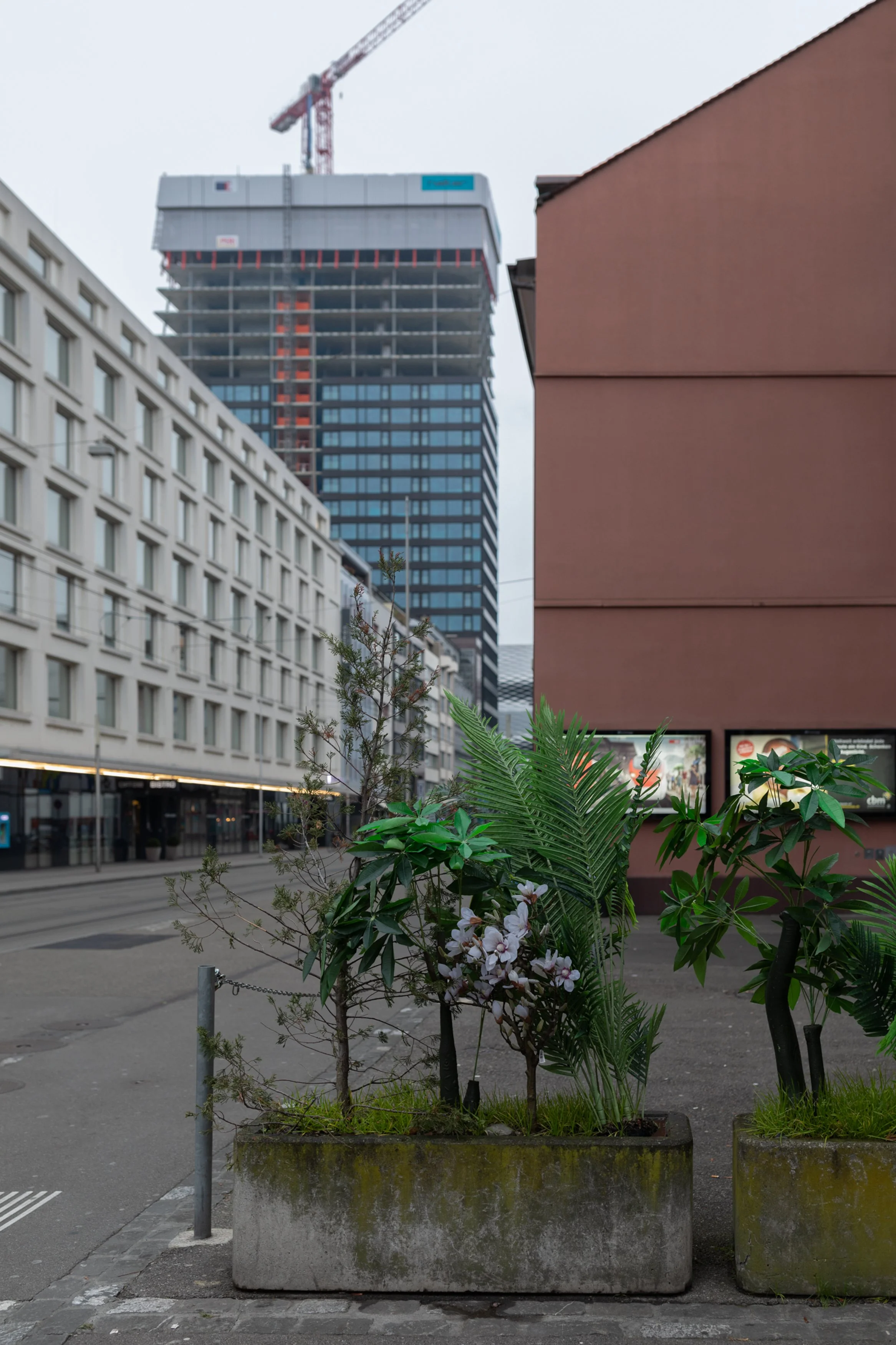 Städtische Szene mit Hochhäusern, Straßenbahngleisen, Pflanzen in Blumentöpfen und einem Gebäude in der Nähe.