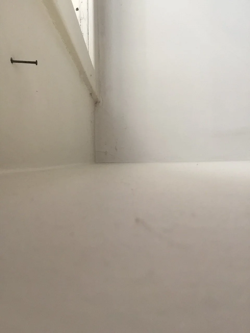 Leerer Raum mit weißen Wänden, ein Teil einer weißen Decke und ein Rohr an der Wand.