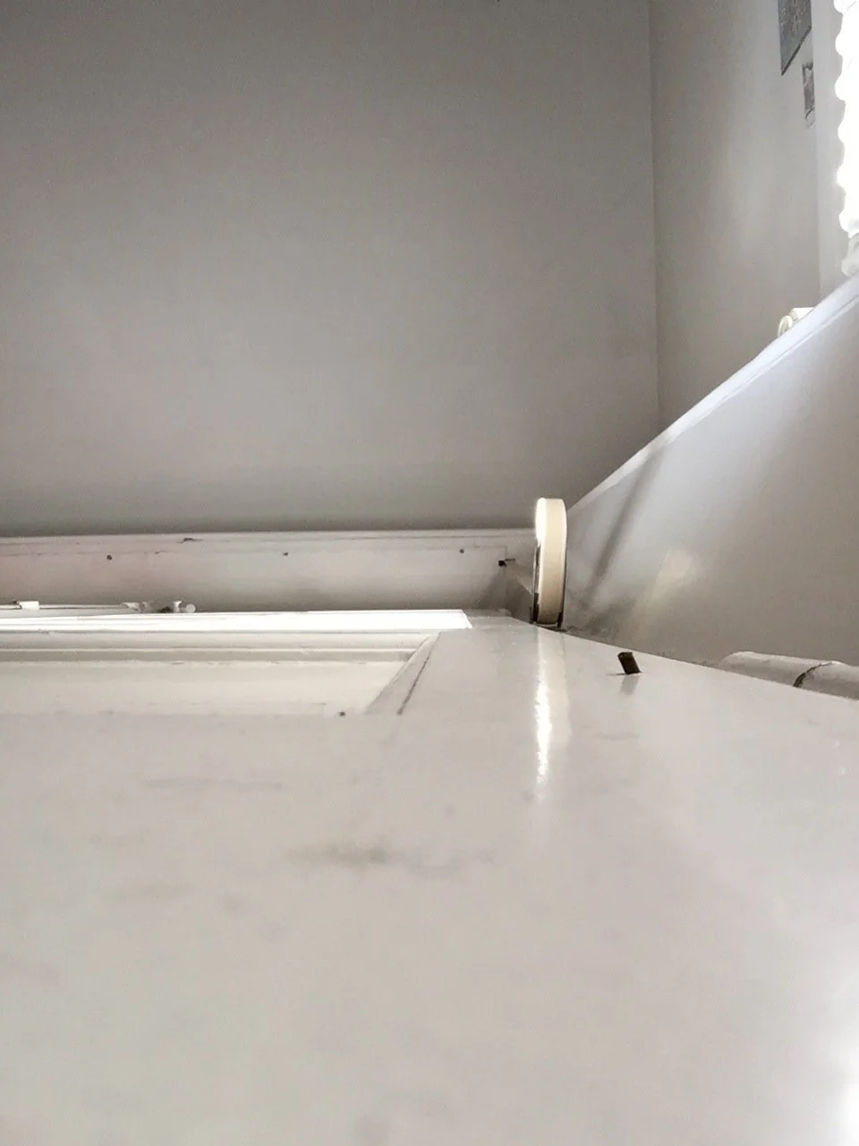 Blick nach oben an einer weißen Tür und einem weißen Türrahmen, mit einer grauen Wand im Hintergrund.