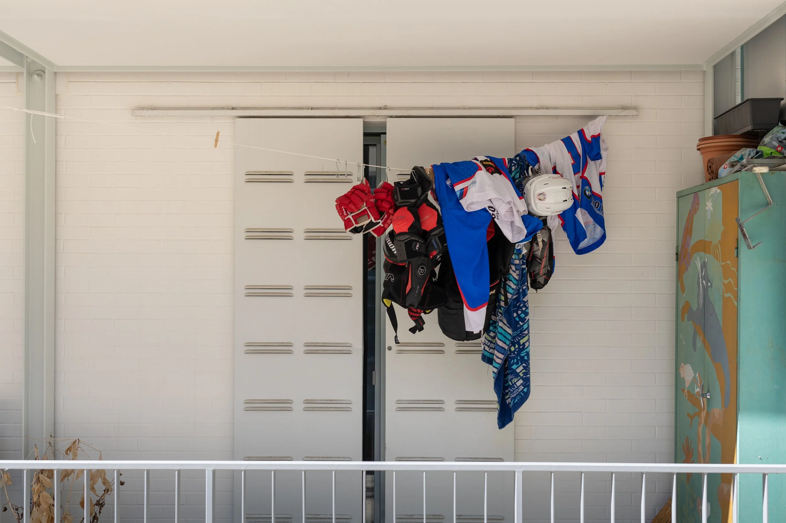 Eine Waschlinie mit Hockeyausrüstung, einschließlich Helme, Handschuhe und Trikots, vor einer weißen Ziegelwand.