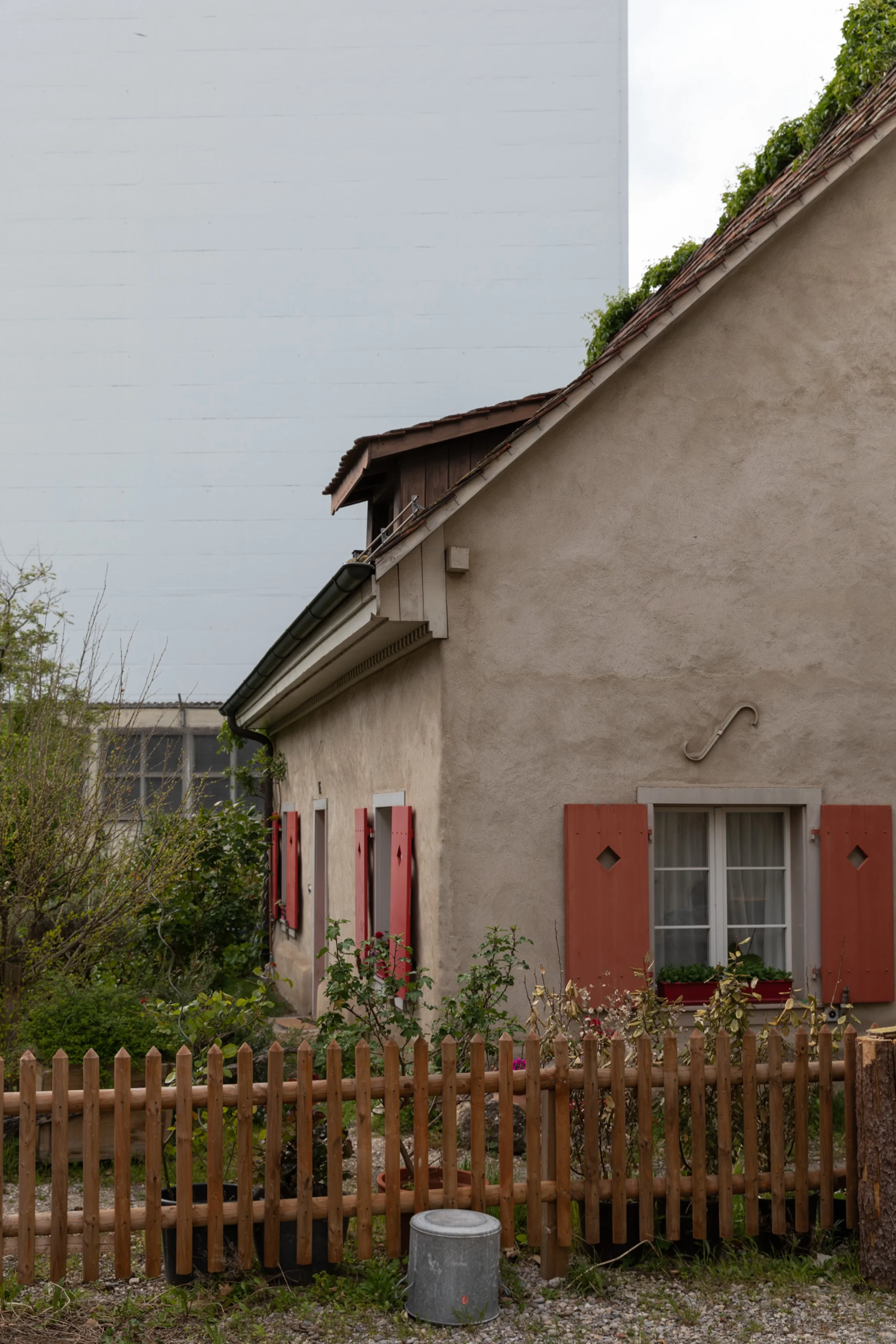 Schmales Haus mit braunen Fensterläden und einem kleinen Garten, eingezäunt mit einem Holzzaun.