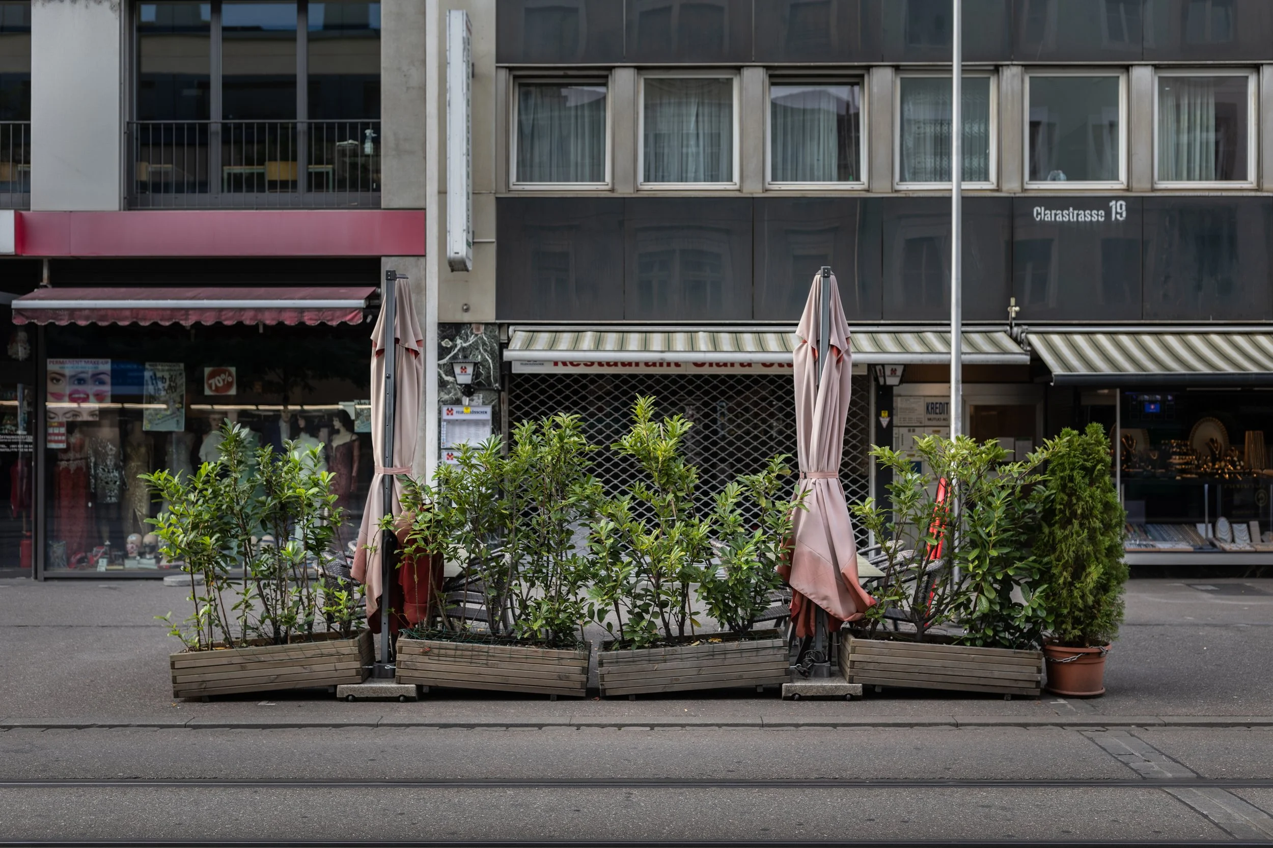 Straßenansicht mit Pflanzkübeln, geschlossene Ladenfront, überdachten Tischen, Umbauarbeiten, geschlossene Geschäfte und einem Gebäude mit mehreren Fenstern, straßenbezogene Beschriftung, Straßennamen, Botschaftsschild, Straßenlaterne