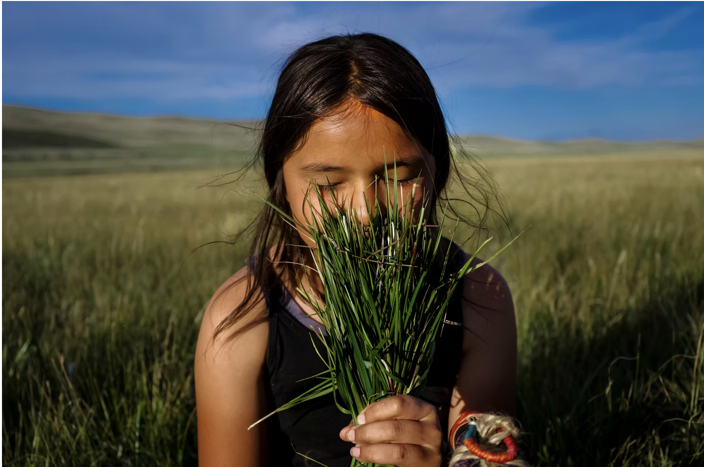 Young Indiginous girl smells sweetgrass bouquet.