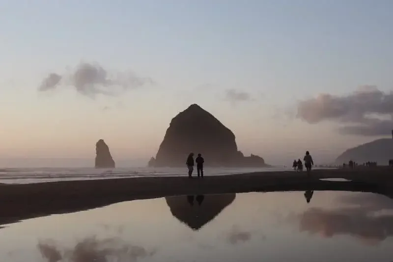 Evening view of Haystack Rock at Cannon Beach, Oregon, with people walking along the shore.