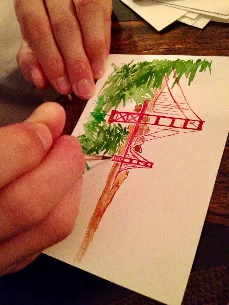Person in an art therapy session drawing a bridge and tree on paper, using colored pencils.