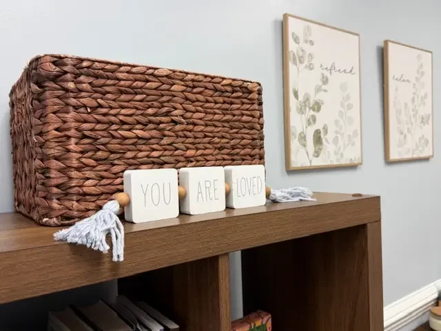 Decorative wicker basket and wooden blocks spelling 'You Are Loved' on a wooden surface in a cozy, well-decorated room at the Firm Foundation Family Services office.