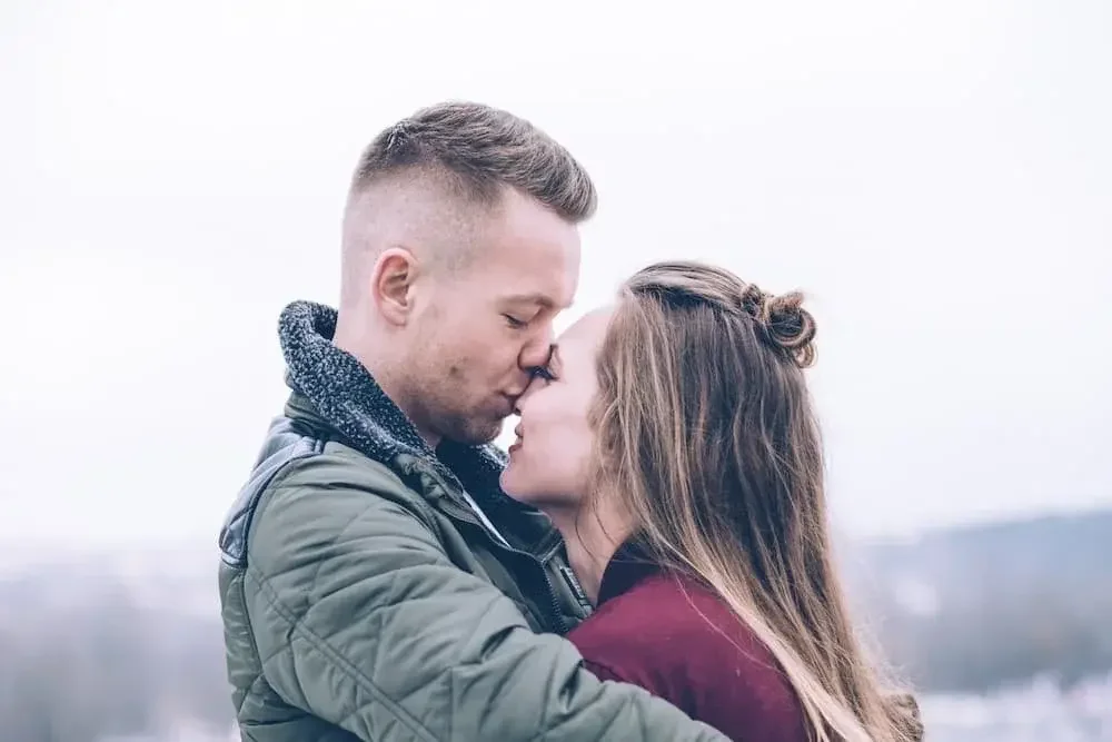 Couple kissing outdoors with a light background.