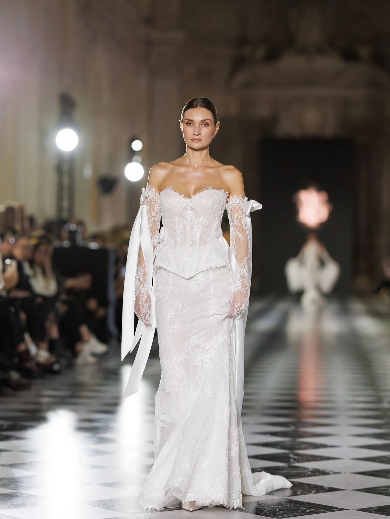 Pure elegance glides down the runway in this exquisite Ricca Sposa wedding gown. 👰&zwj;♀️✨ The off-the-shoulder neckline, intricate lace details, and dramatic ribbon-tie sleeves create a breathtakingly romantic and unforgettable bridal look. 🤍 @ric