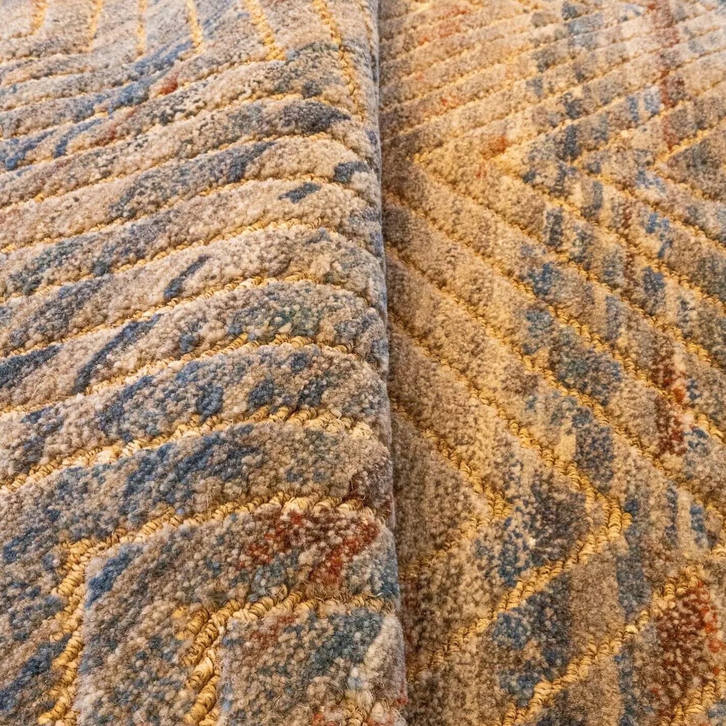 The Hiho rug features a linear pattern that spans the entire piece, with zigzags revealing hidden hues of blue, red, and brown. From afar, the rug appears muted and cohesive, while up close, its textures take center stage.
