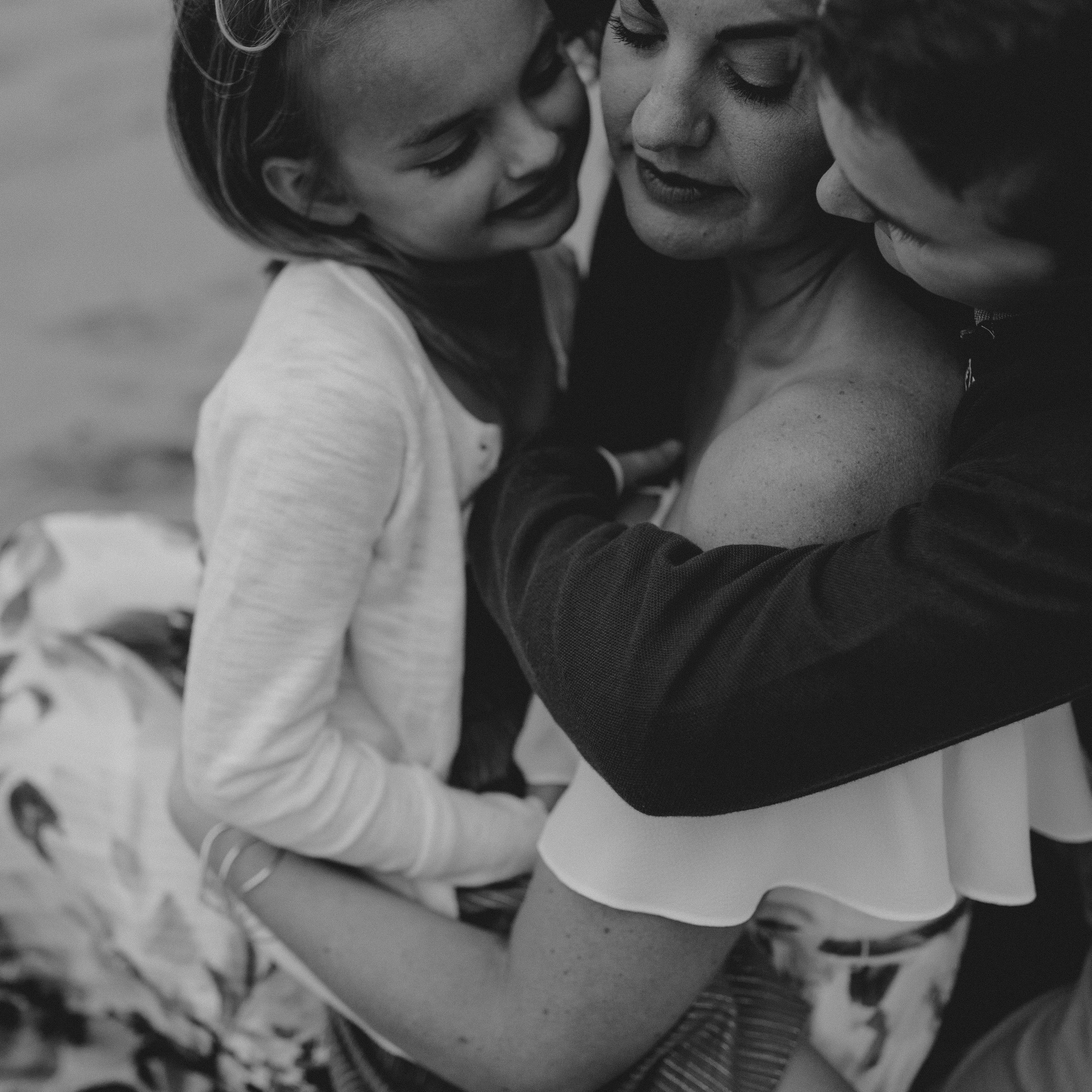pretty mom with son and daughter giving snuggles and love black and white family photo.jpg