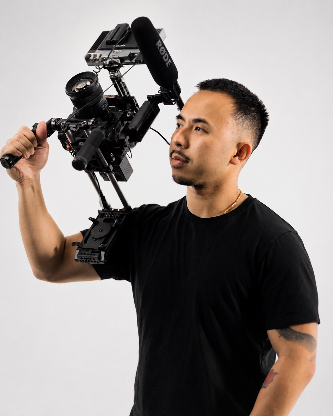 Man holding a professional video camera on his shoulder against a plain white background.