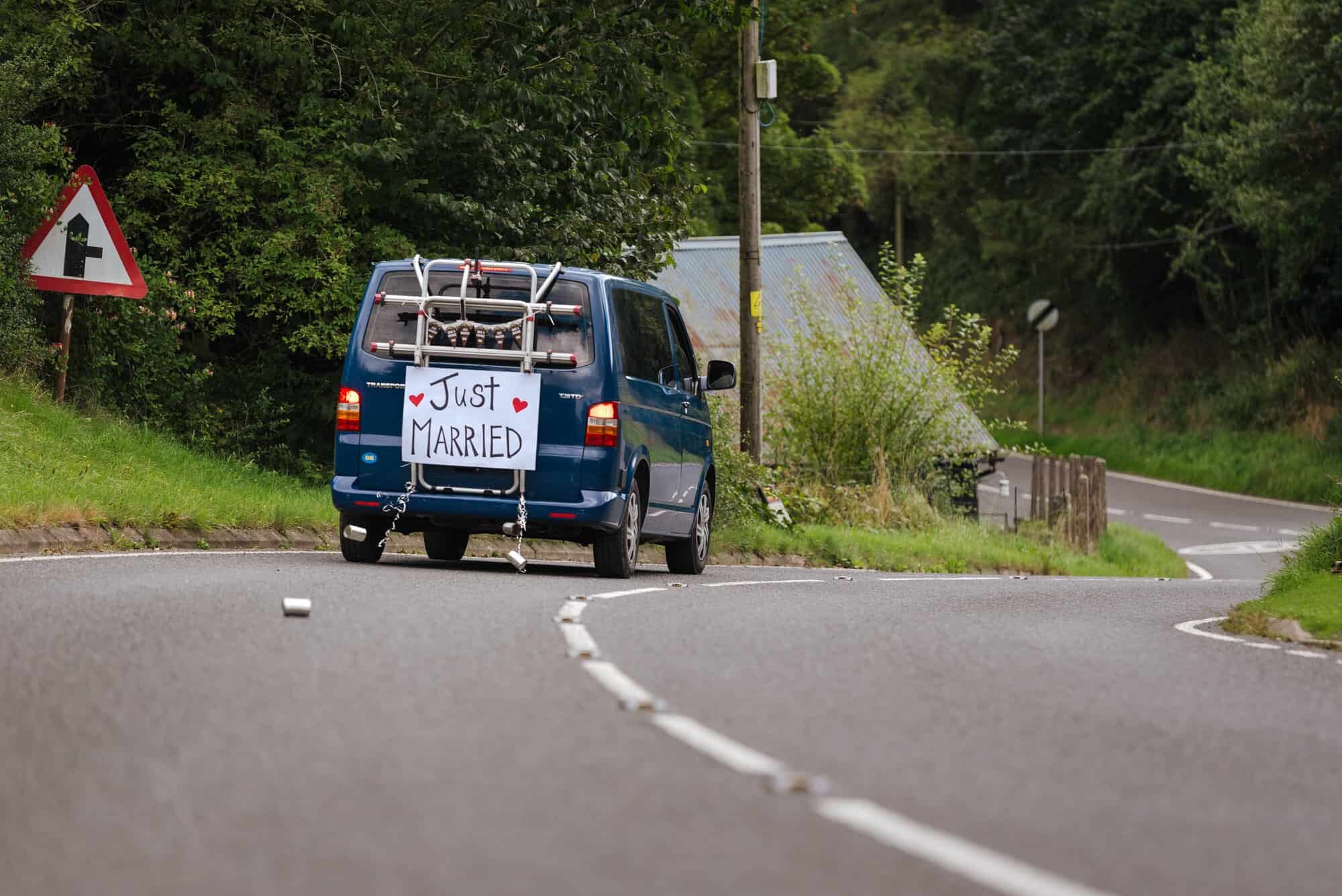 Van leaving wedding with cans tied to the back and sign saying Just Married