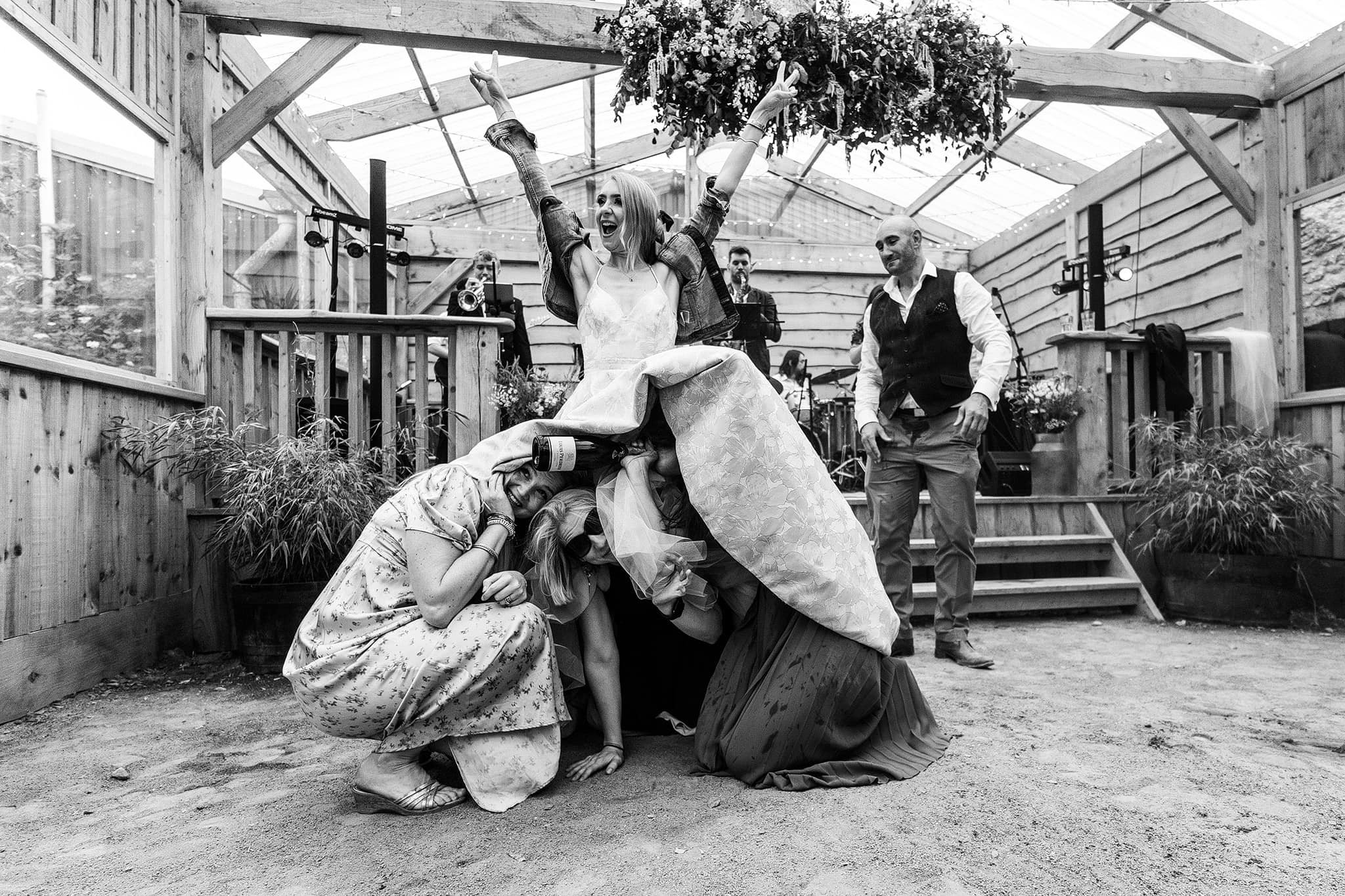 Bride with arms in the air and guests under wedding dress at Holford Arms