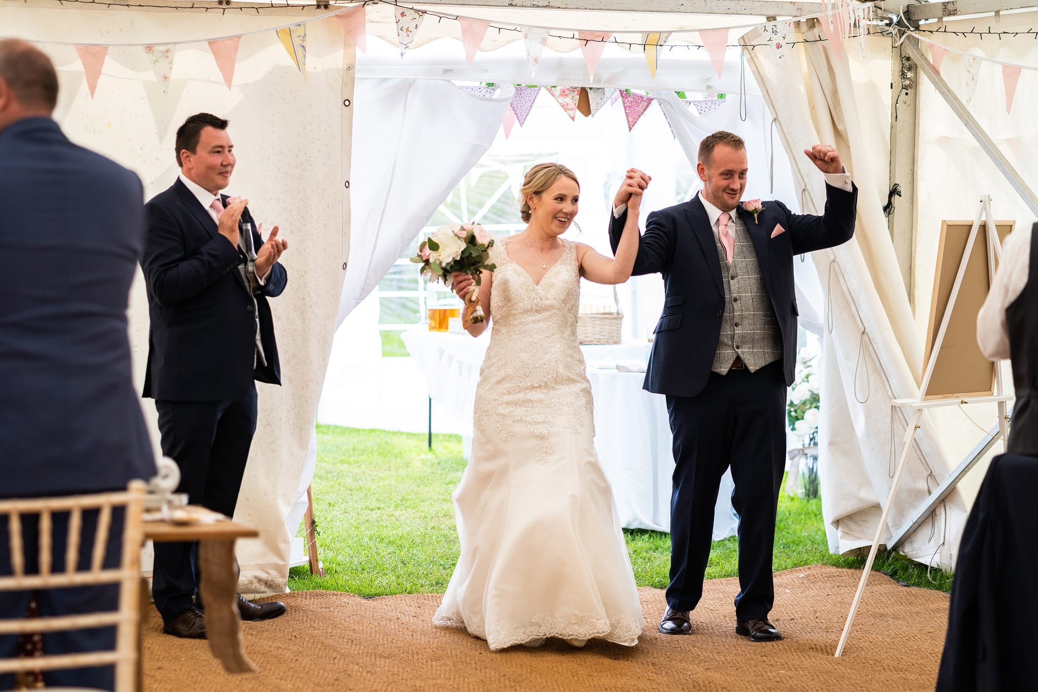 Groom and Bride with arms up celebrating as walk into reception