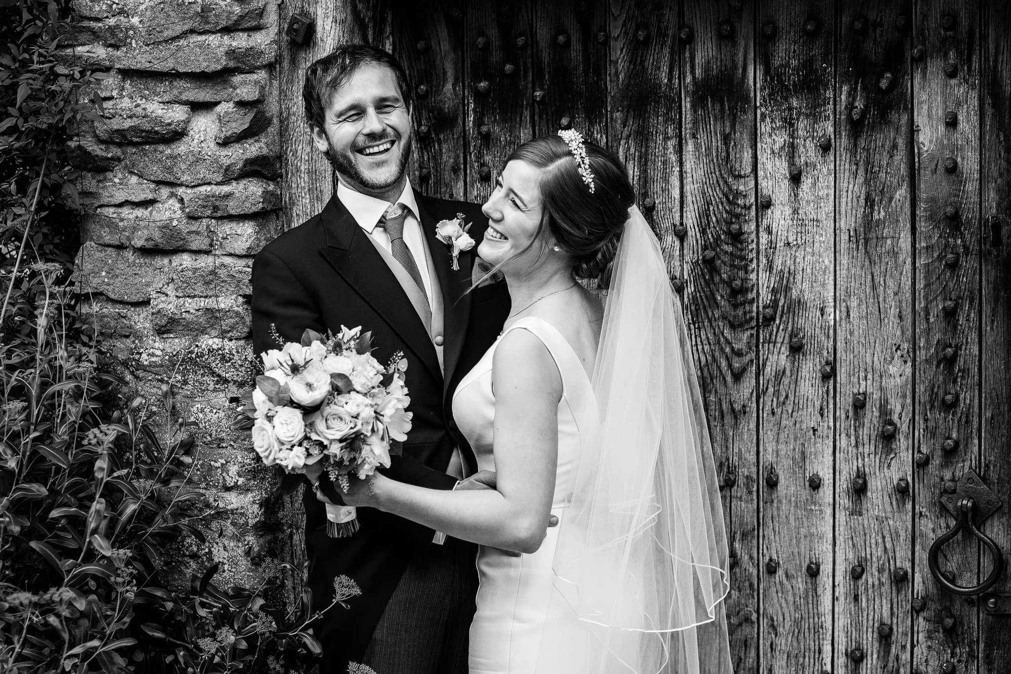 Bride and groom laughing in doorway at Dewsall Court