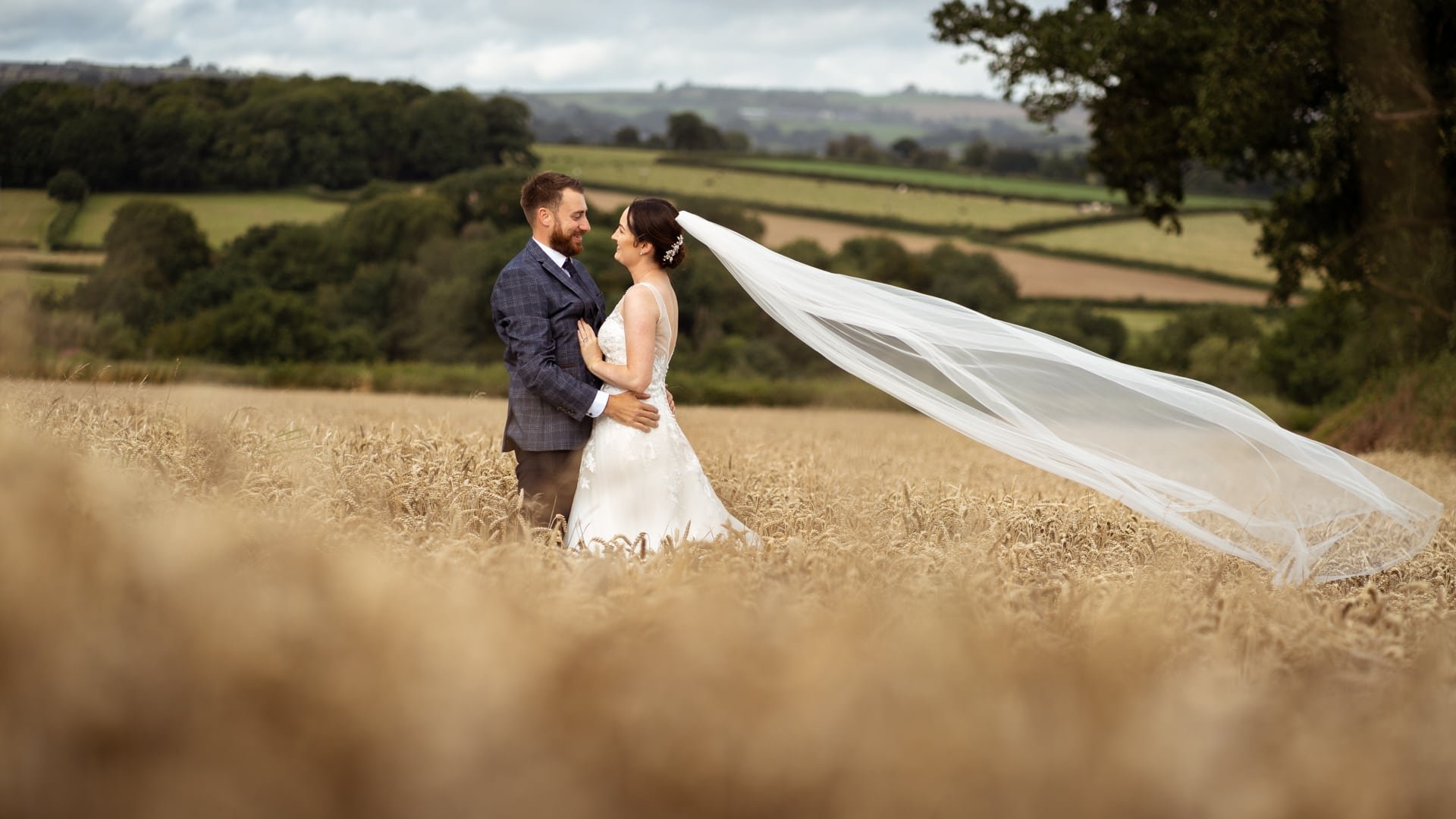 Bride &amp; groom in field with veil blowing in wind