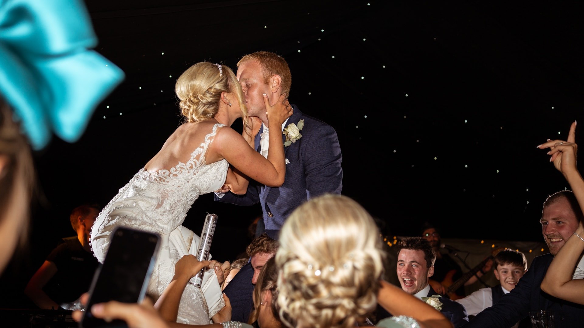 Bride &amp; groom on shoulders kissing during wedding party