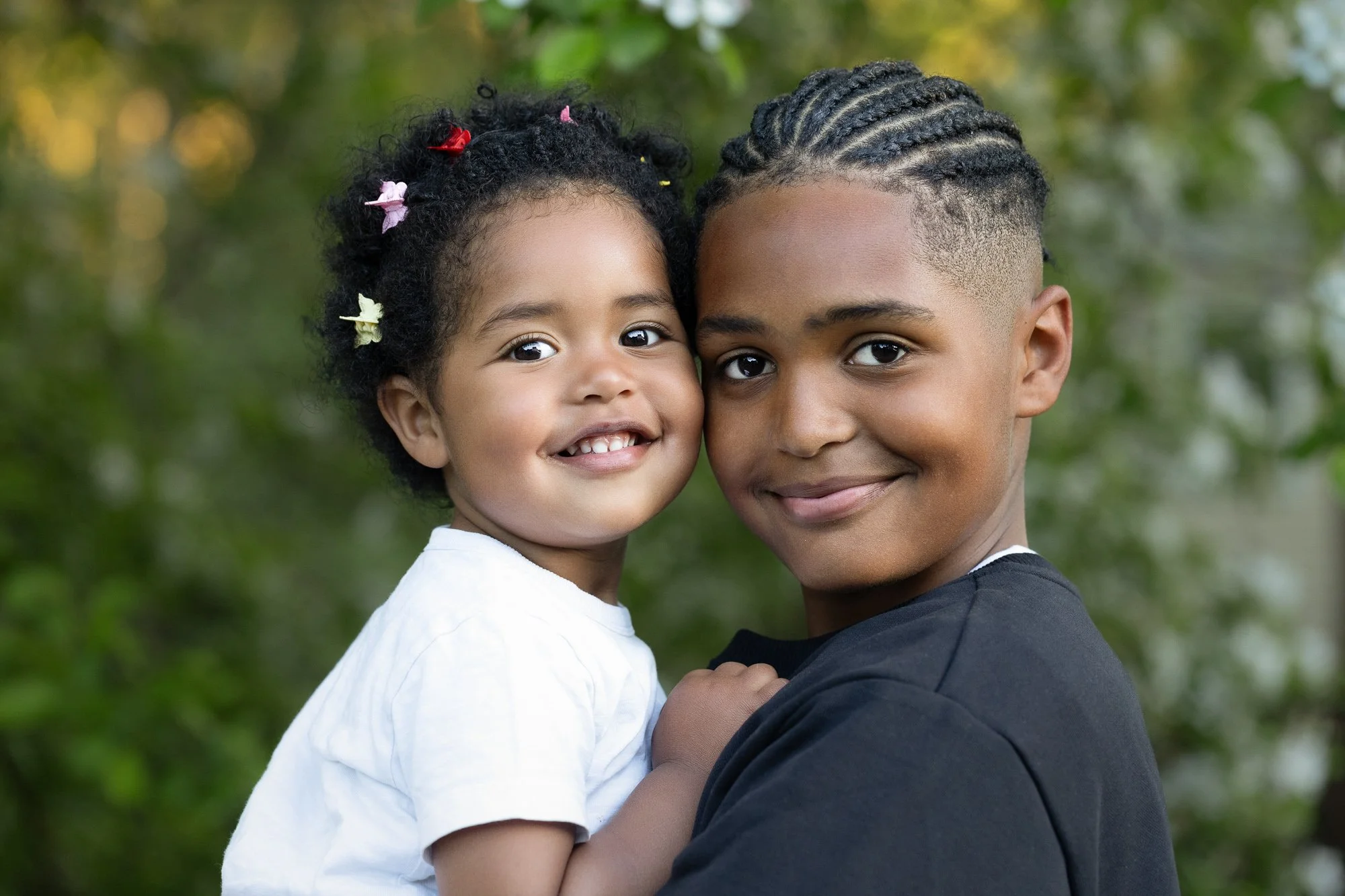 brother and toddler sister, in close embrace, photographed with a blurred out green foiliage background