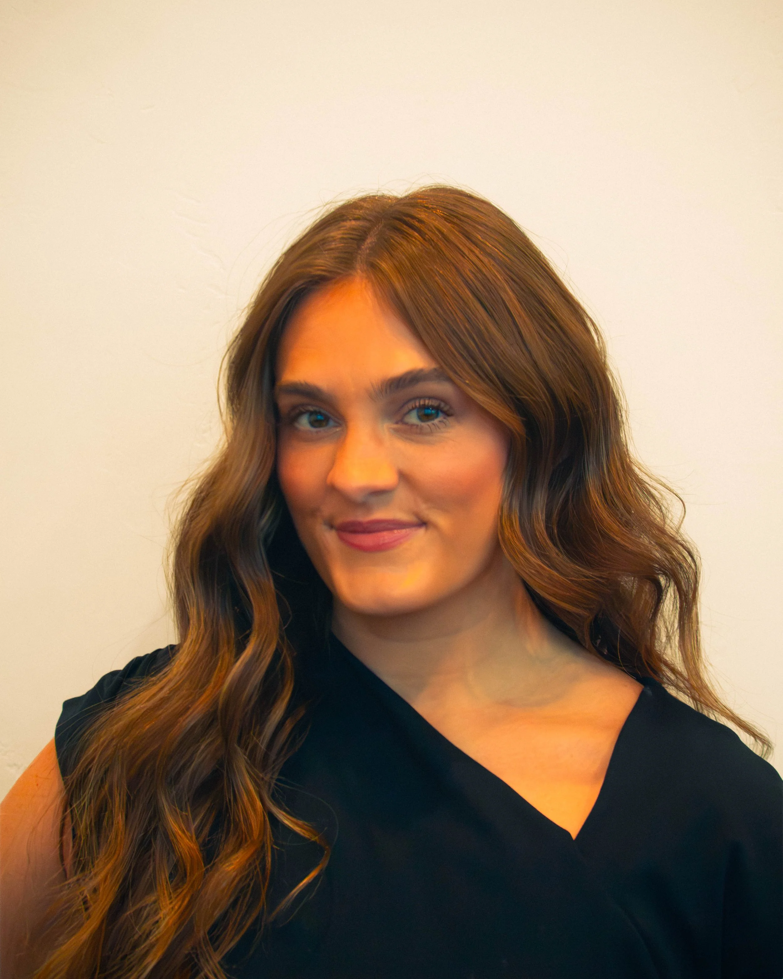 Woman with long brown hair smiling in a black top, close-up portrait.