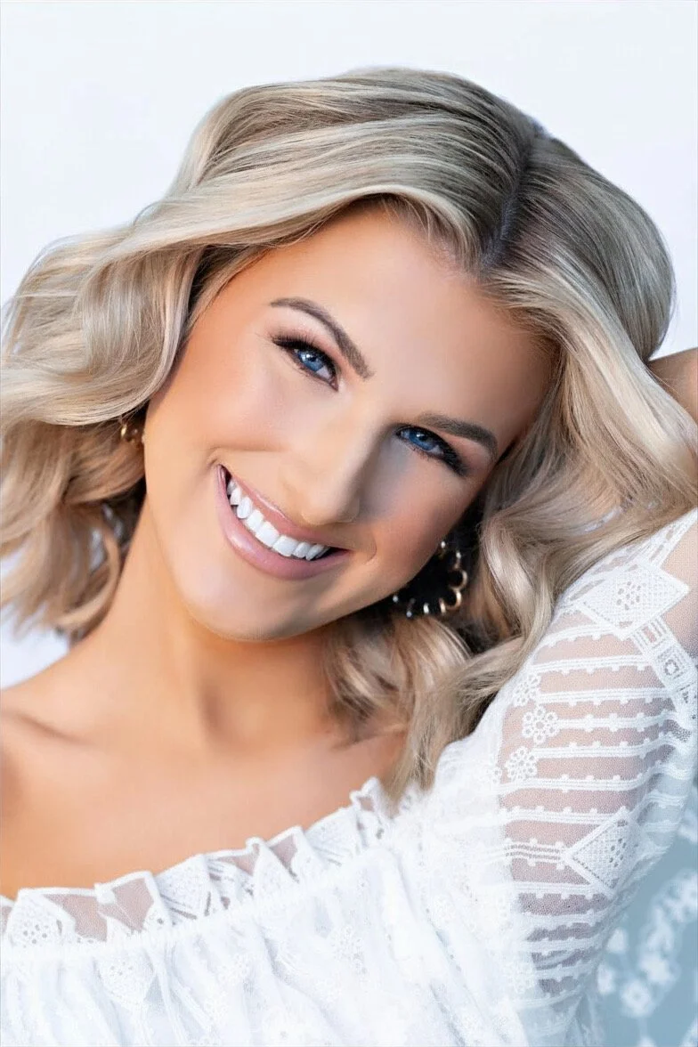 Smiling person with wavy blonde hair and a white textured top