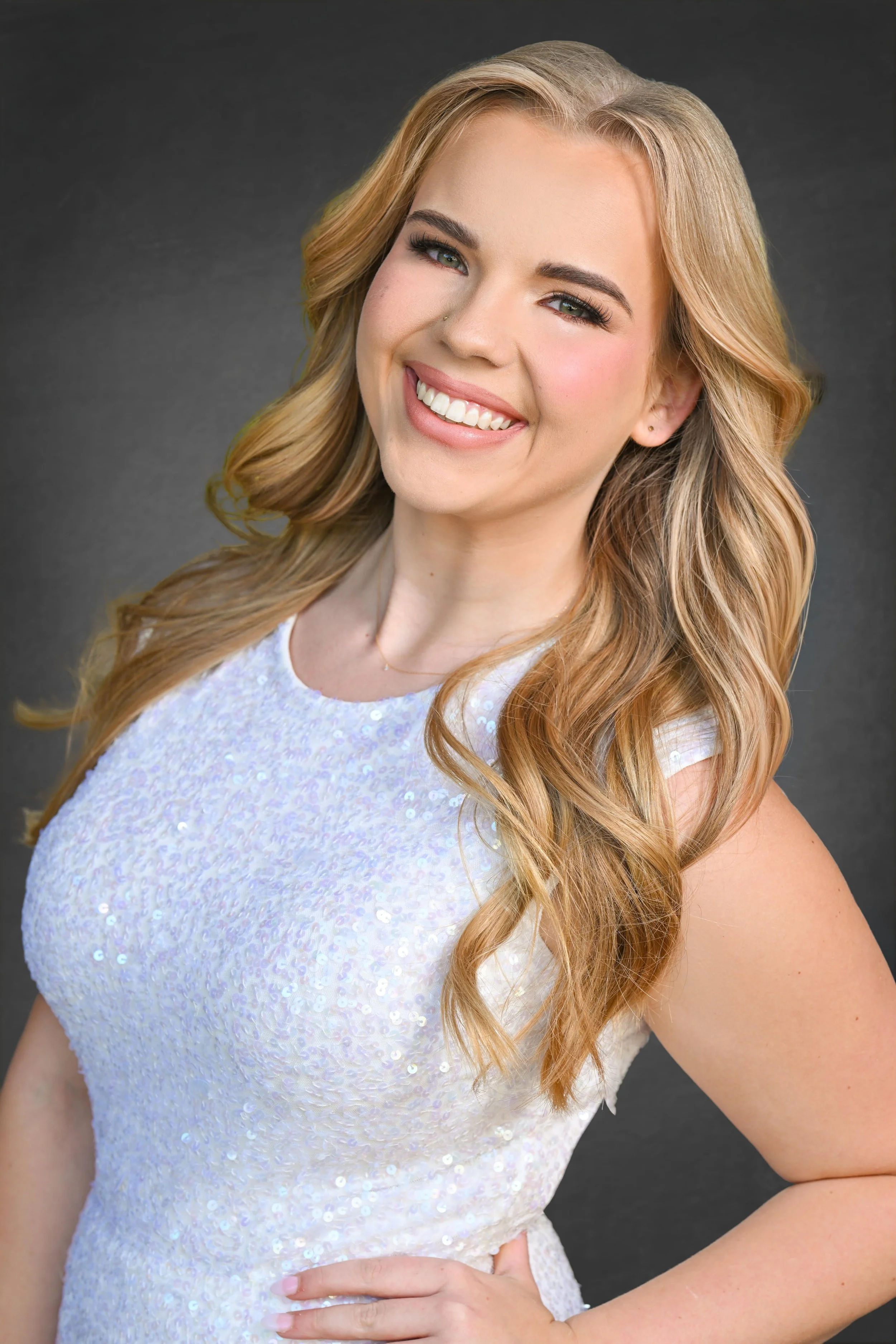 Smiling woman with curly blonde hair wearing a white dress and hoop earrings.