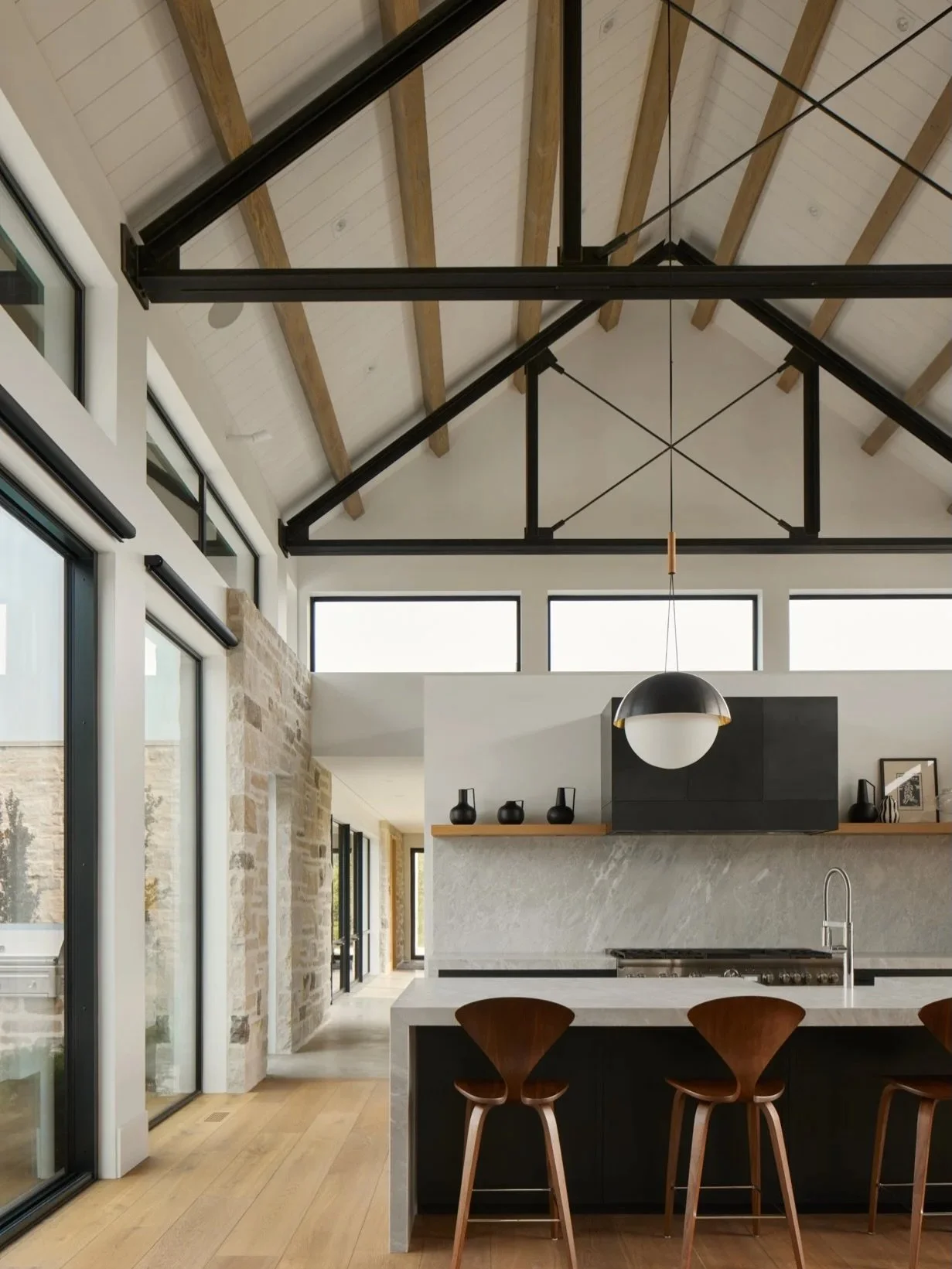Soft white walls and ceilings shape an ethereal greatroom at Lacuna, becoming the canvas for punctuated moments of stone, steel, and wood. Delicate steel trusses lend scale to the expansive volume, while stone and wood touch points soften the spaces 