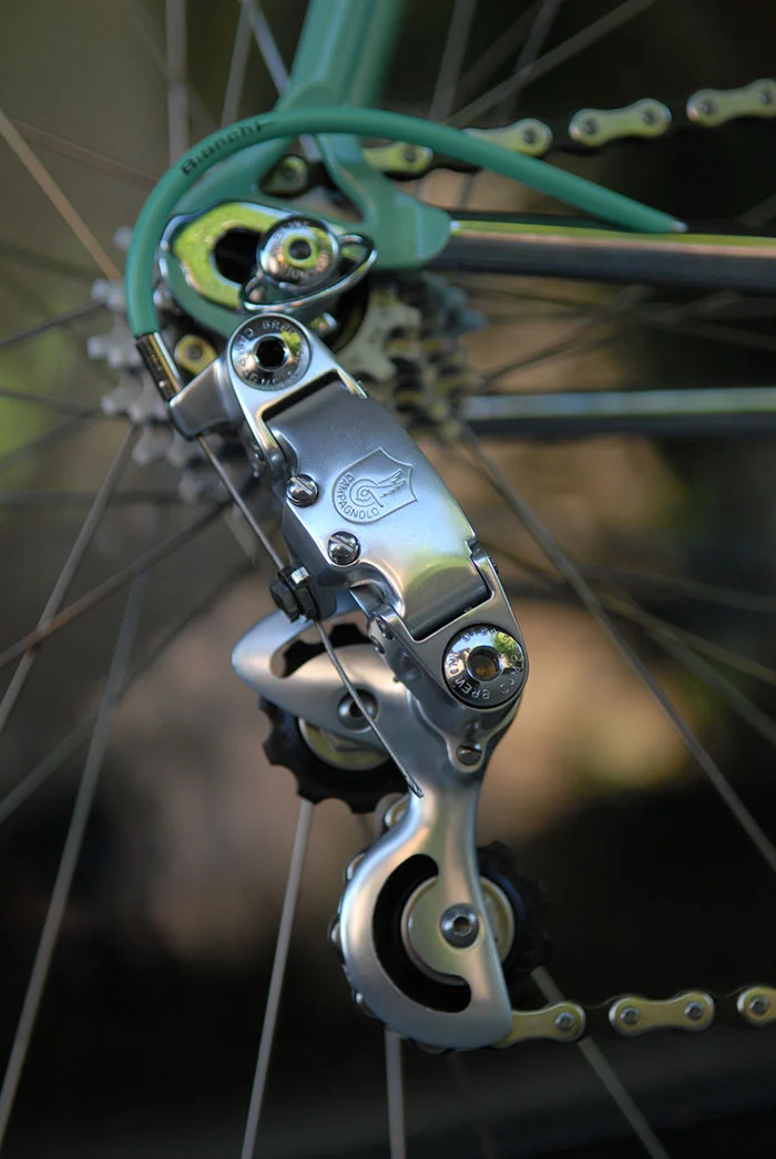 There were three versions of the Gen 1 Campagnolo C Record rear derailleur. This rear mech is the third cage type with slots cutout in the top and the bottom of the cage. The other type had only the bottom part of the cage cutout and the most well known version had no cutouts. This cutout version is sometimes referred to as a Gen 1.5 Corsa Record rear mech.