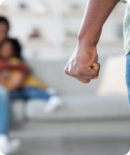 Person with clenched fist, with a blurred woman sitting on a couch in the background.