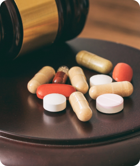 Various pills and capsules on a dark surface with a wooden container in the background.