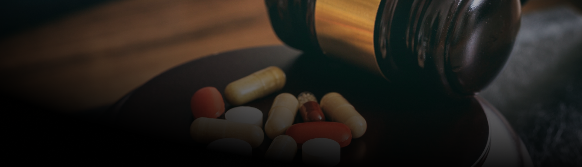 Pills spilled from a brown bottle onto a dark surface