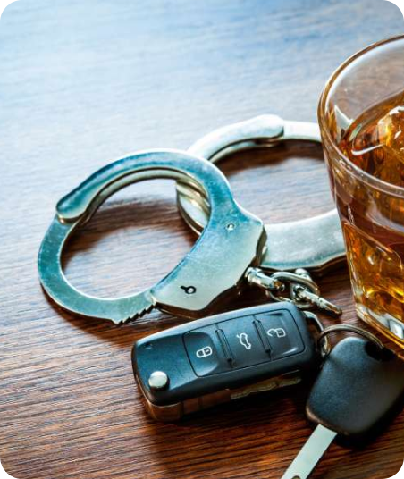Handcuffs, car key, and a glass of whiskey on a wooden surface.