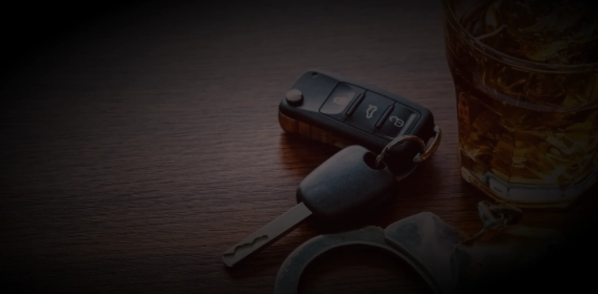 Close-up of a car key, a glass of whiskey, and some other items on a wooden surface.