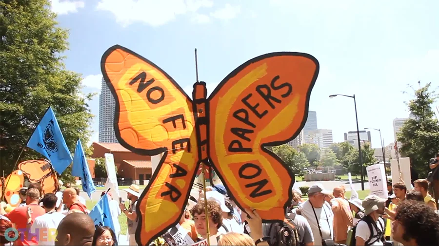 The image of the butterfly, created by Favianna, is now used by immigration activists across the nation. Image is a cardboard butterfly which reads "No Fear, No Papers" on the wings. It is being held at a march. Image via Raconteur.la