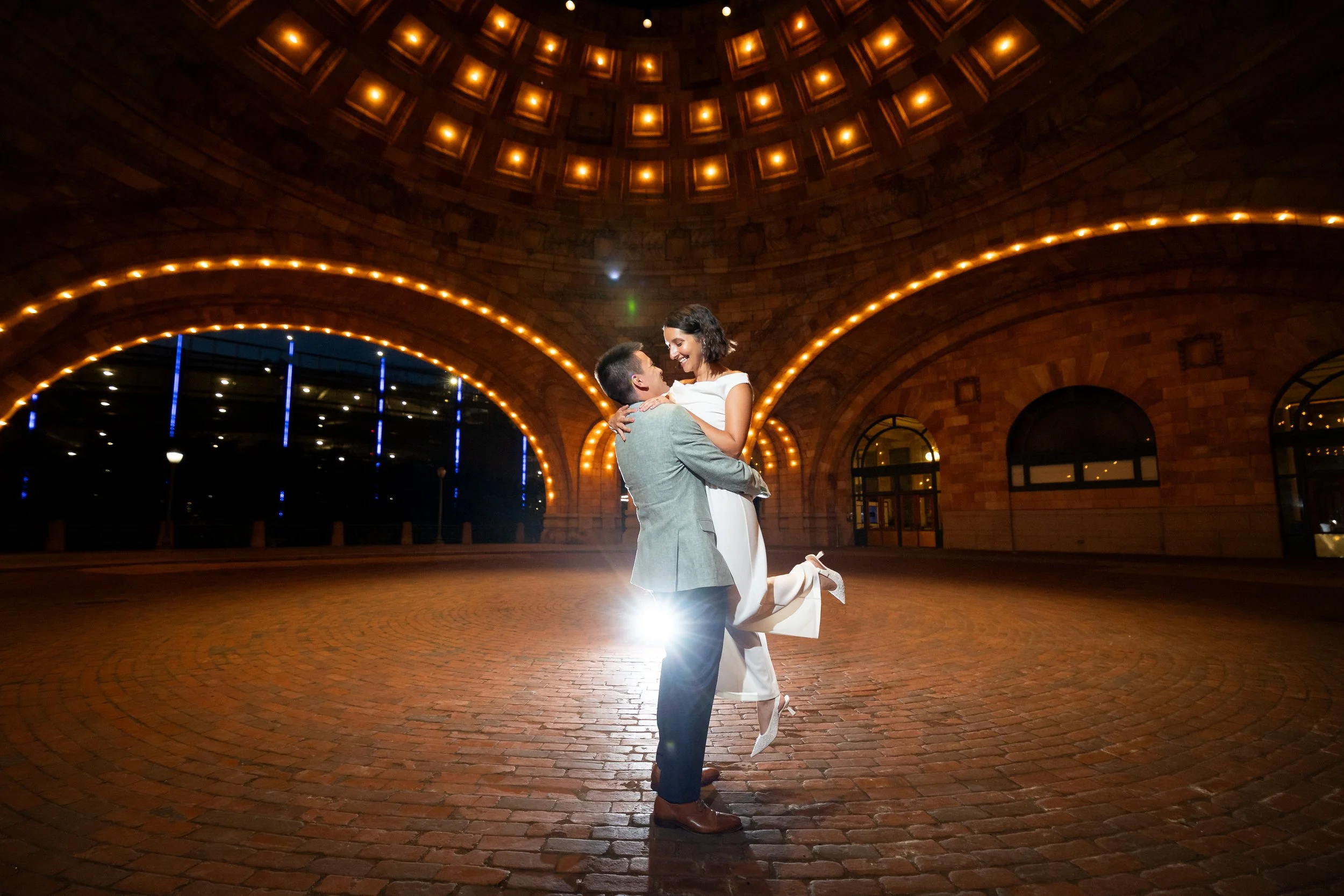 A happy couple dancing in an arched brick building with warm lighting, at night.