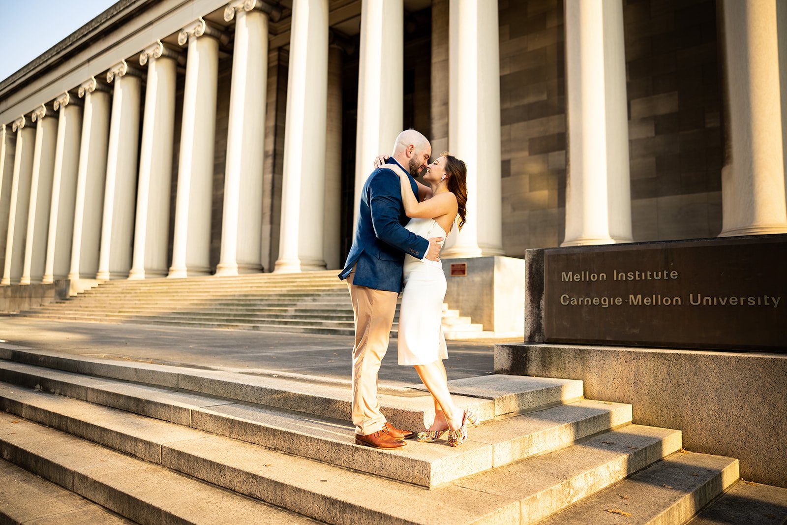 A couple embracing on the steps outside the Mellon Institute at Carnegie-Mellon University, with classical columns in the background.