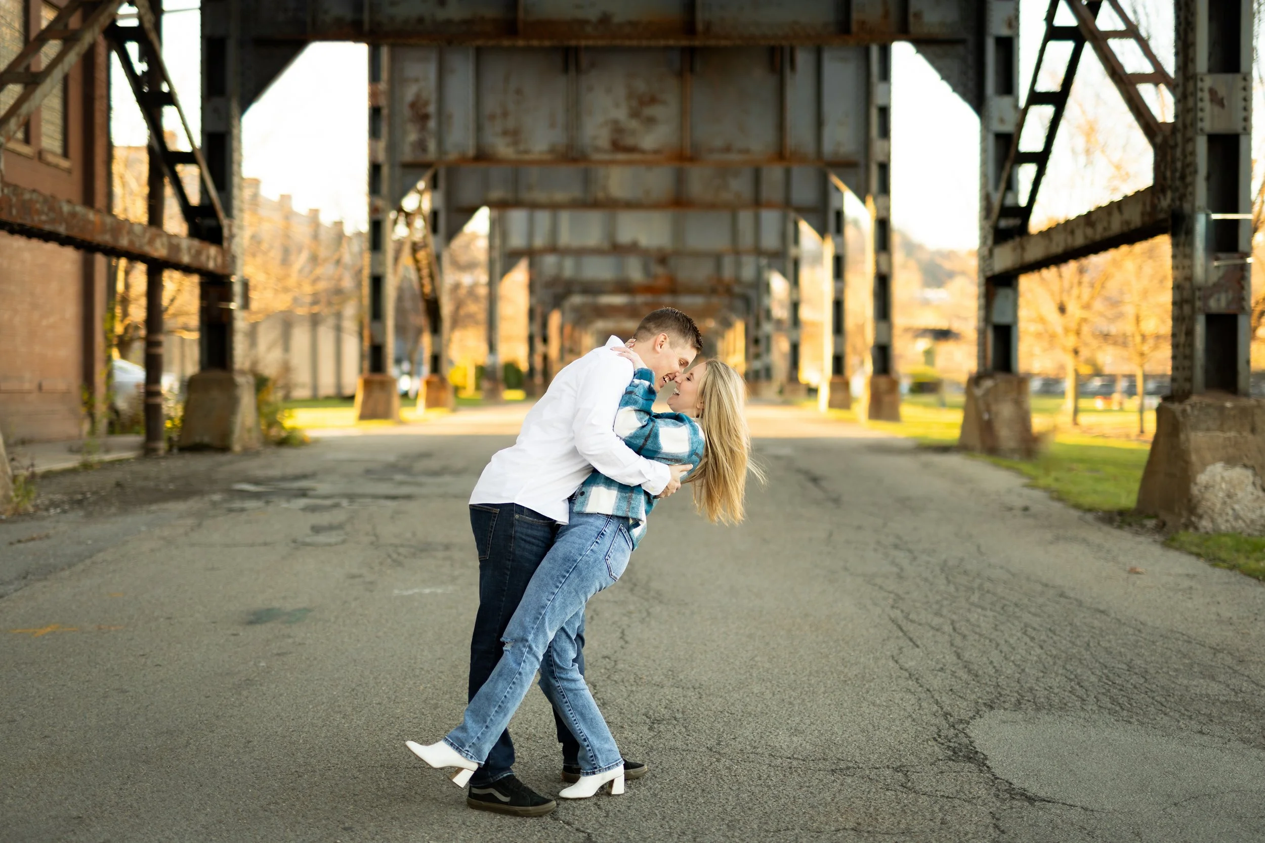 A couple sharing a dance on an empty street during sunset, with an industrial bridge structure overhead.