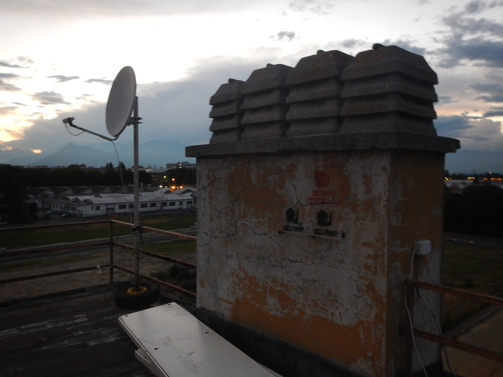 Sunset shot from the rooftop at Via Madonna delle Salette, the latest building to be occupied to host the refugees. The rooftop offers an amazing sunset view over the mountain chain that surrounds the city of Turin, while the satellite dish installed brings its inhabitants closer to home. On the wall, the logo of the solidarity committee: a snail with a closed fist as the shell.