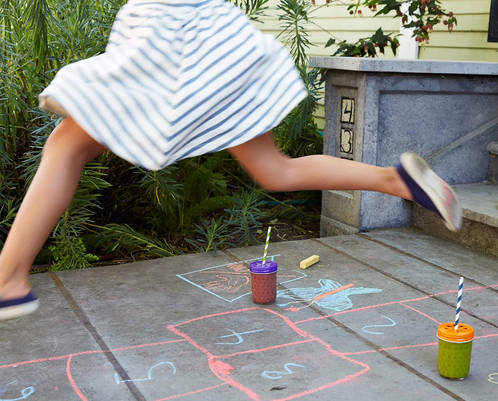 girl playing hopscotch on sidewalk with smoothies